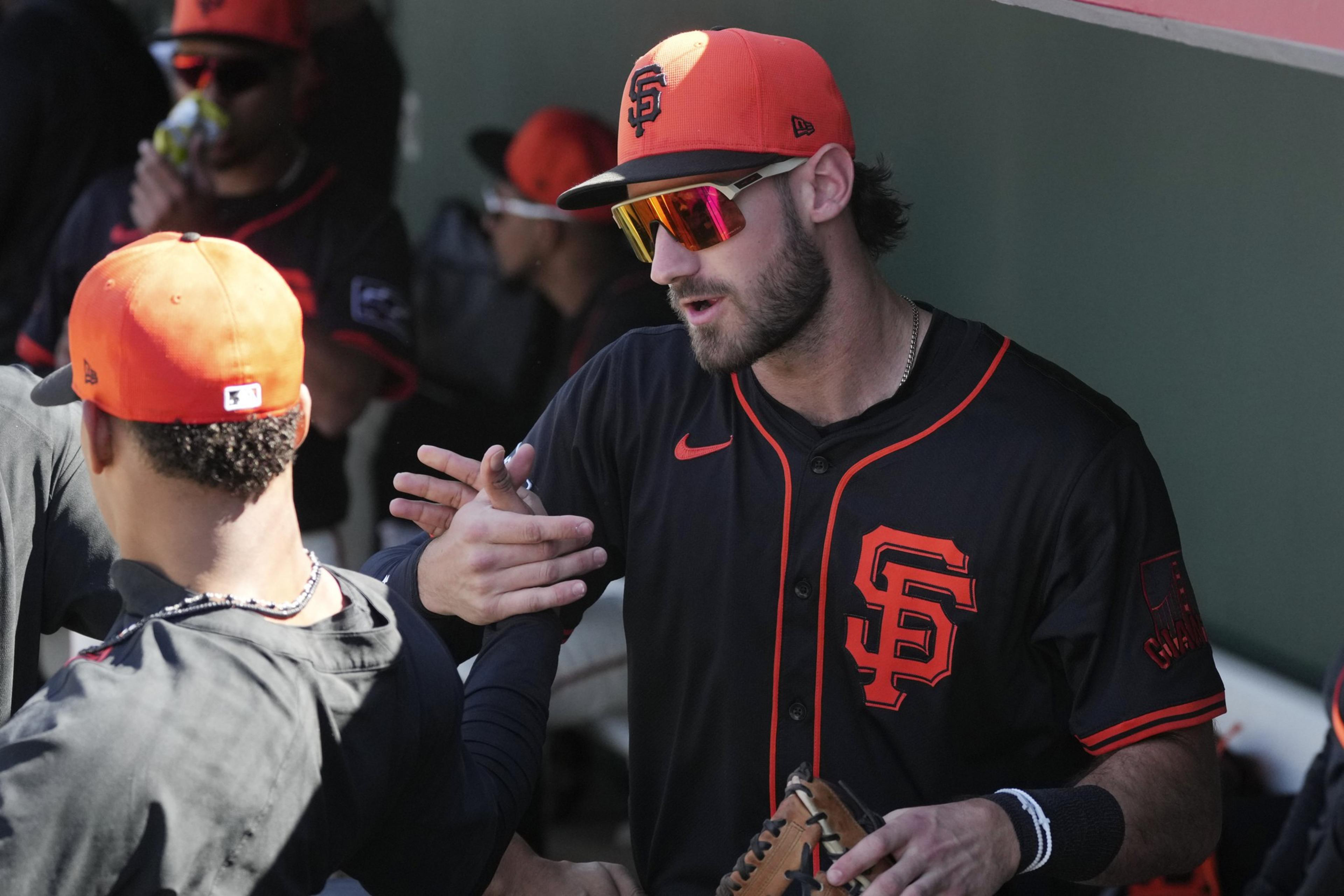 A baseball player wearing a black and orange uniform and cap with &quot;SF&quot; on it is giving a handshake in the dugout. He's holding a glove and wearing sunglasses.