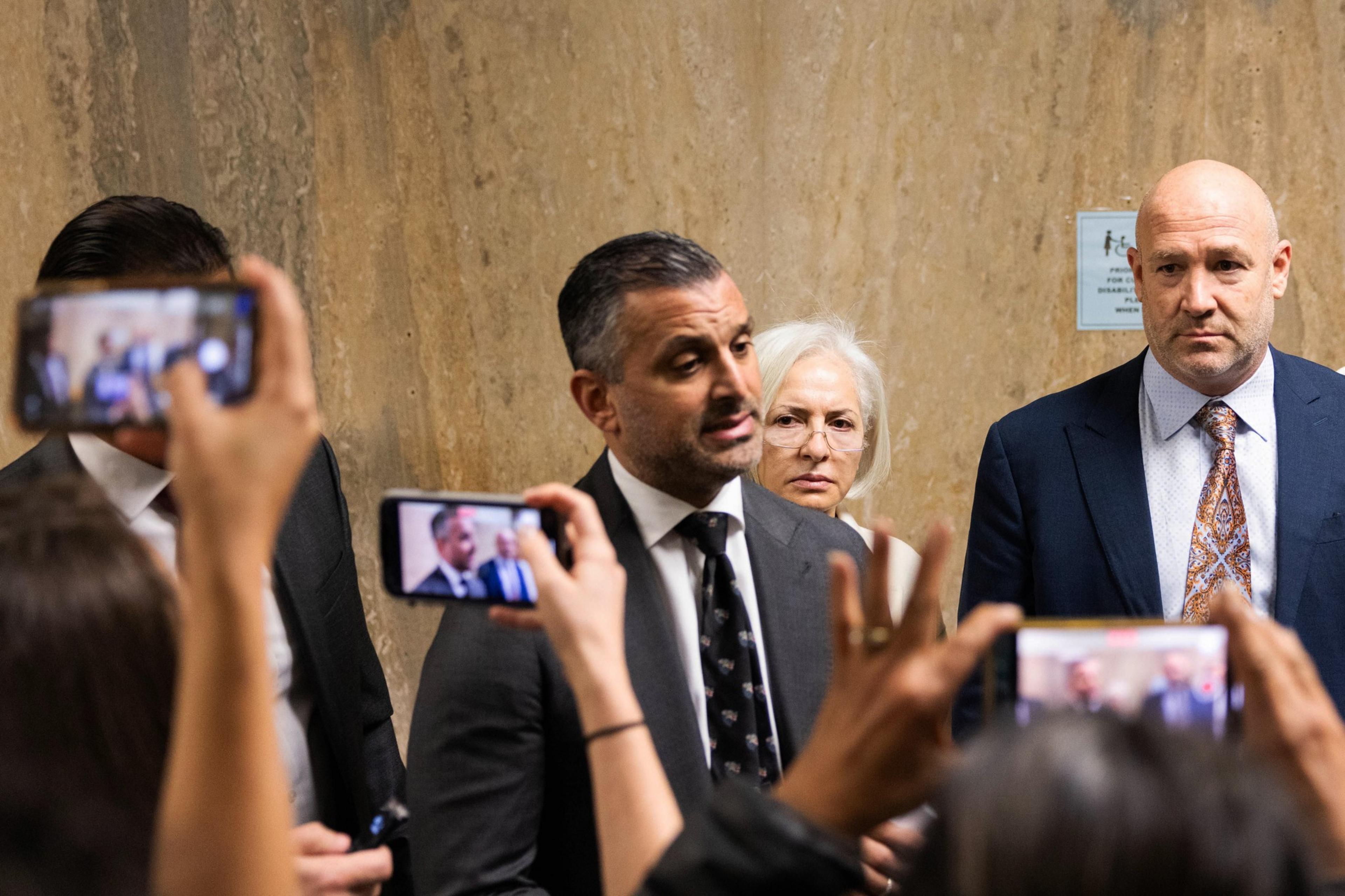 Saam Zangeneh, one of Momeni’s lawyers, addresses the media with 2 other lawyers standing beside him as members of the media record the press conference with their iphones