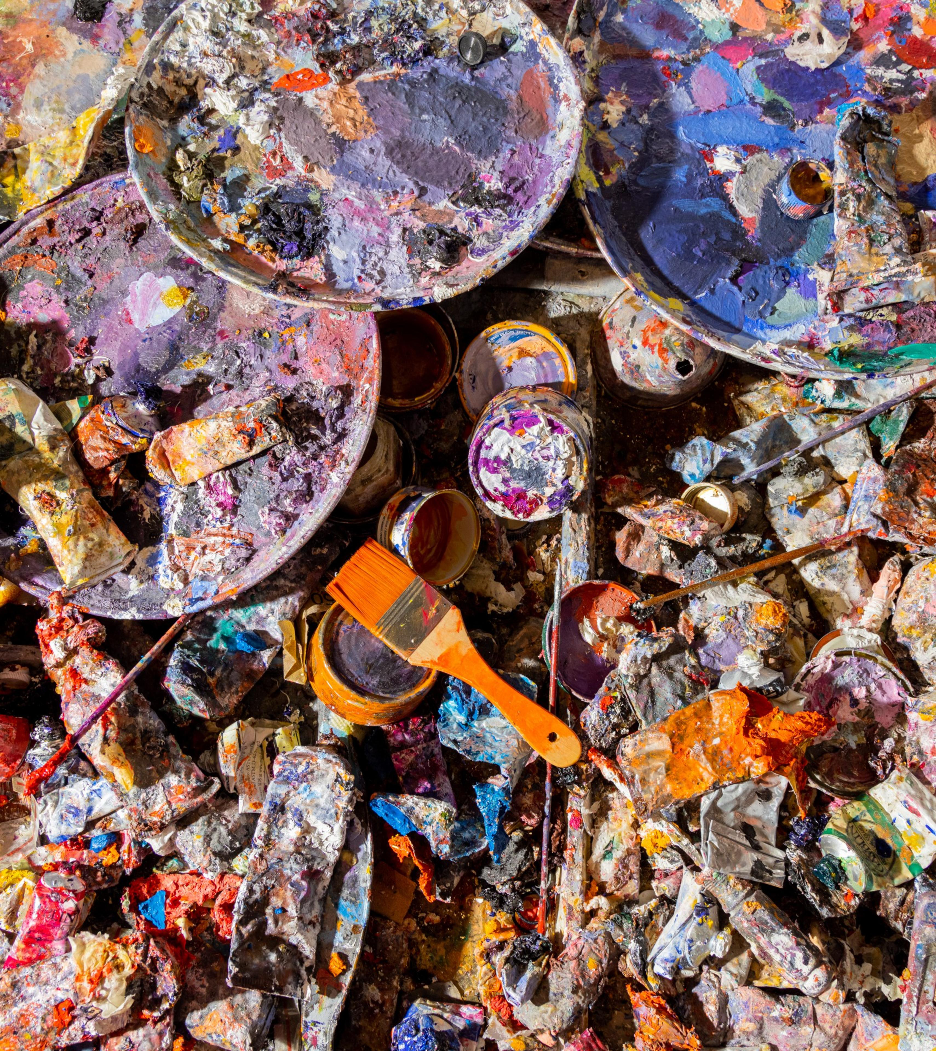 A cluttered array of used paint tubes, palettes, and brushes, caked with colorful dried paint.