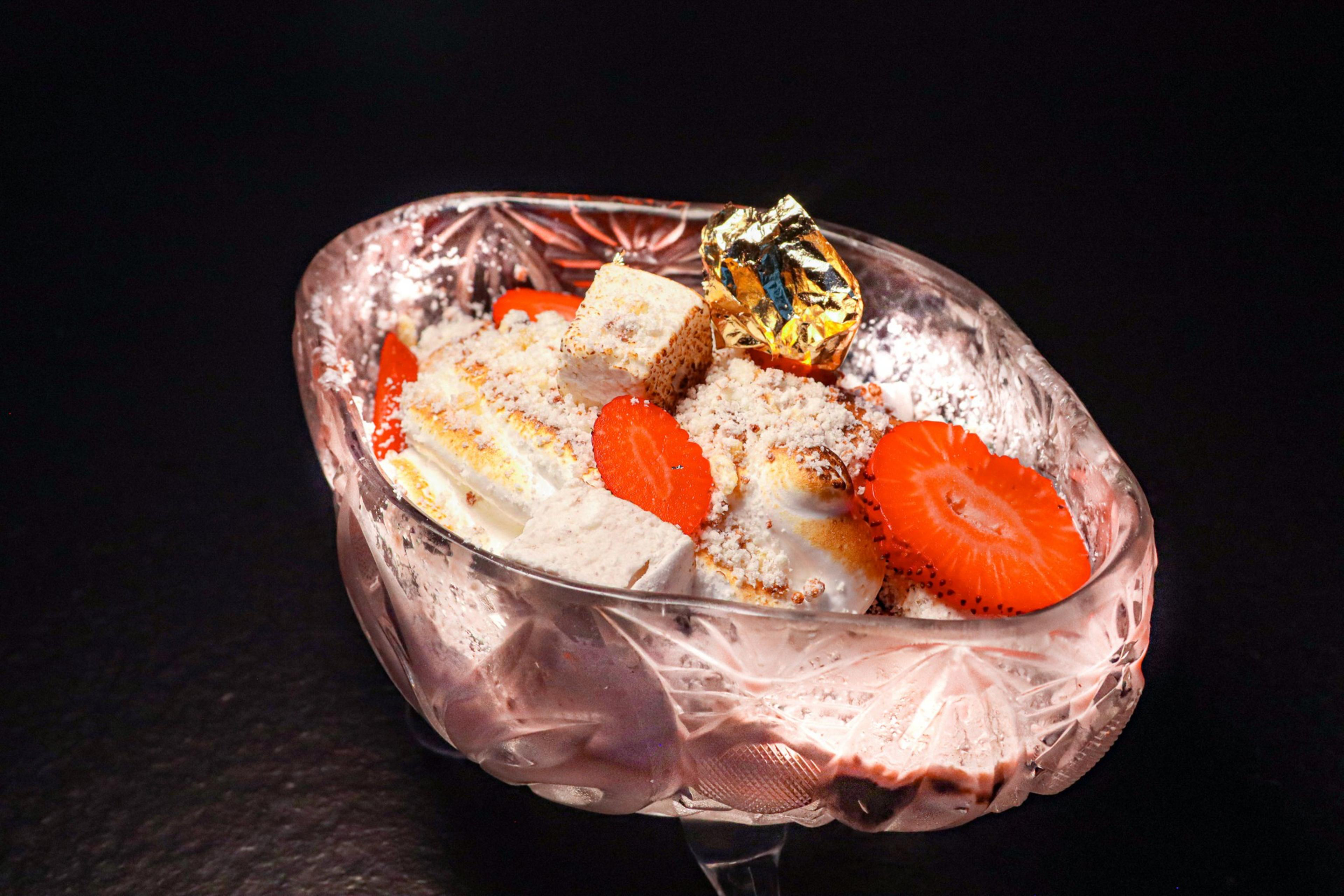 A shave ice dessert in an asymmetrical bowl topped with strawberries and gold flake.