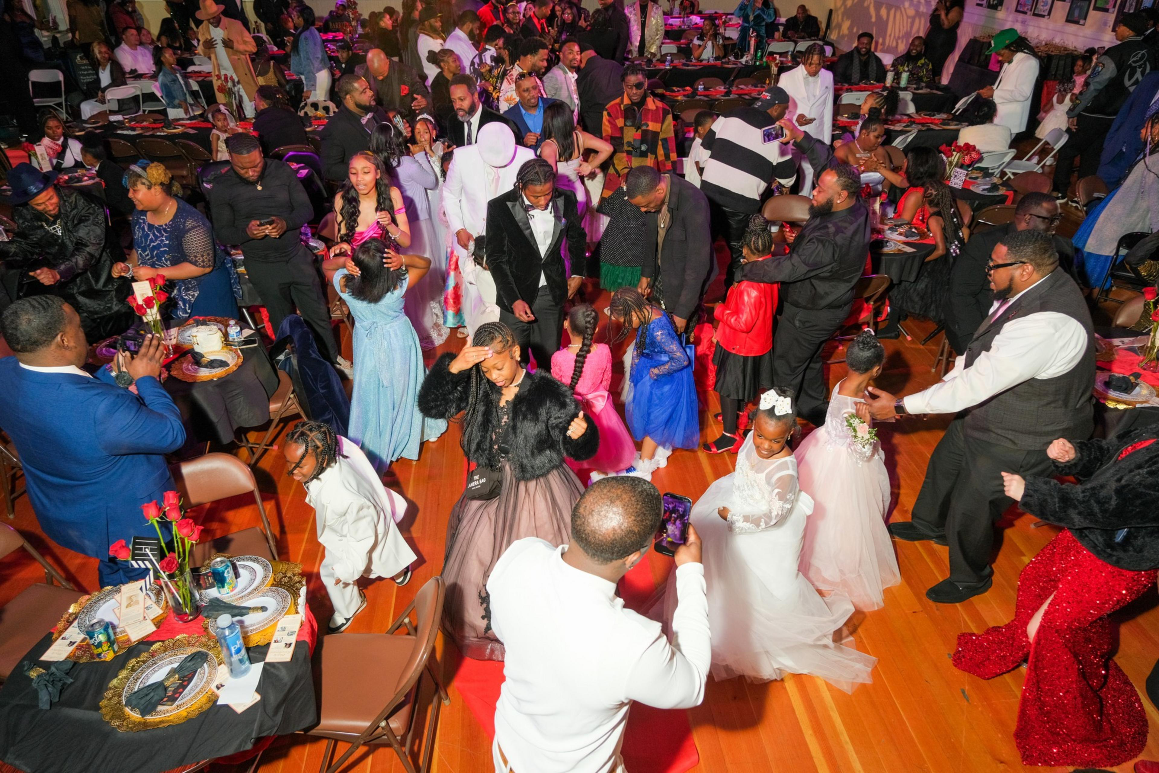 A lively indoor celebration with elegantly dressed adults and children mingling and dancing.
