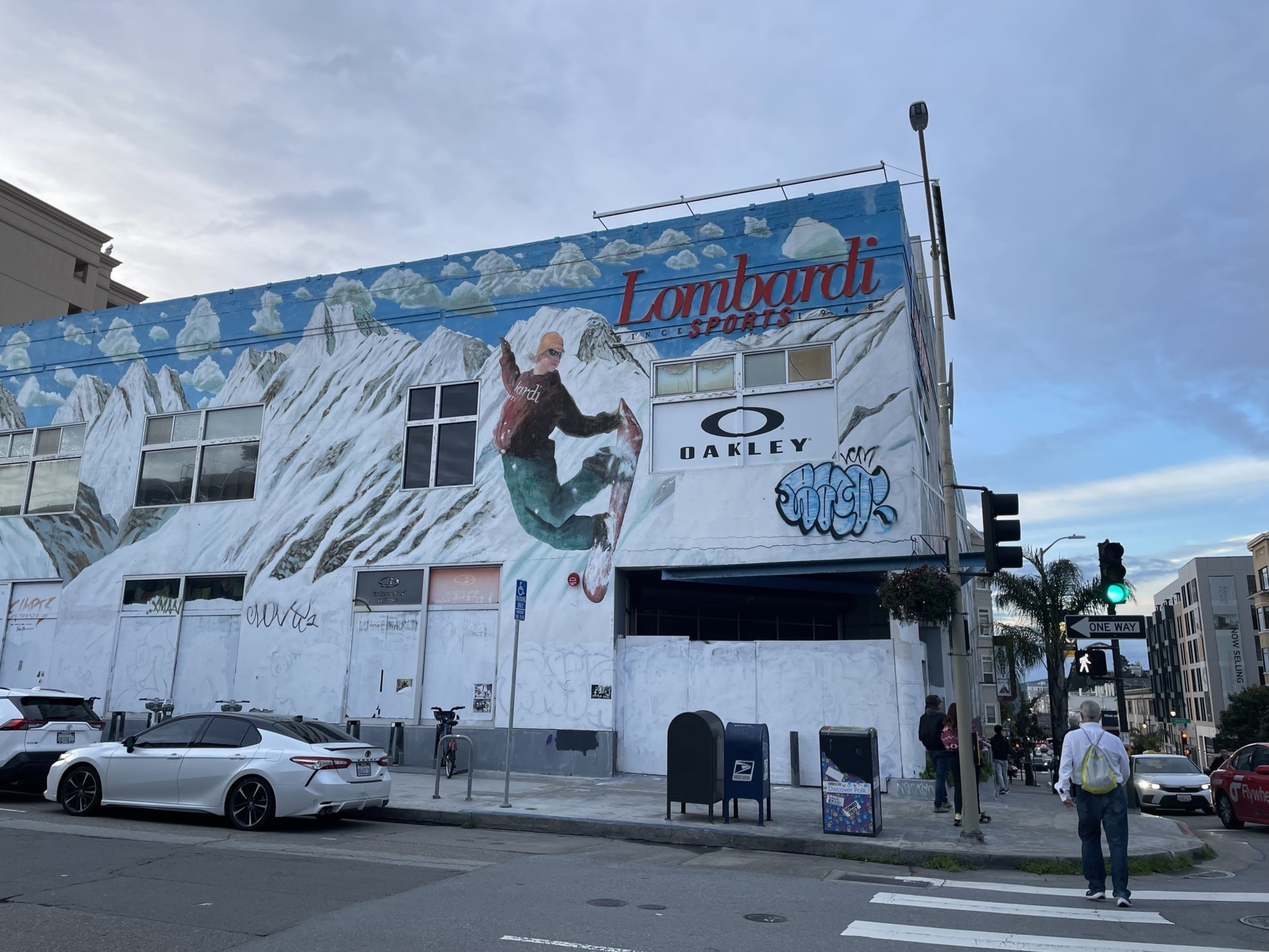 People walk past a large, empty retail building covered in a mural depicting winter sports.
