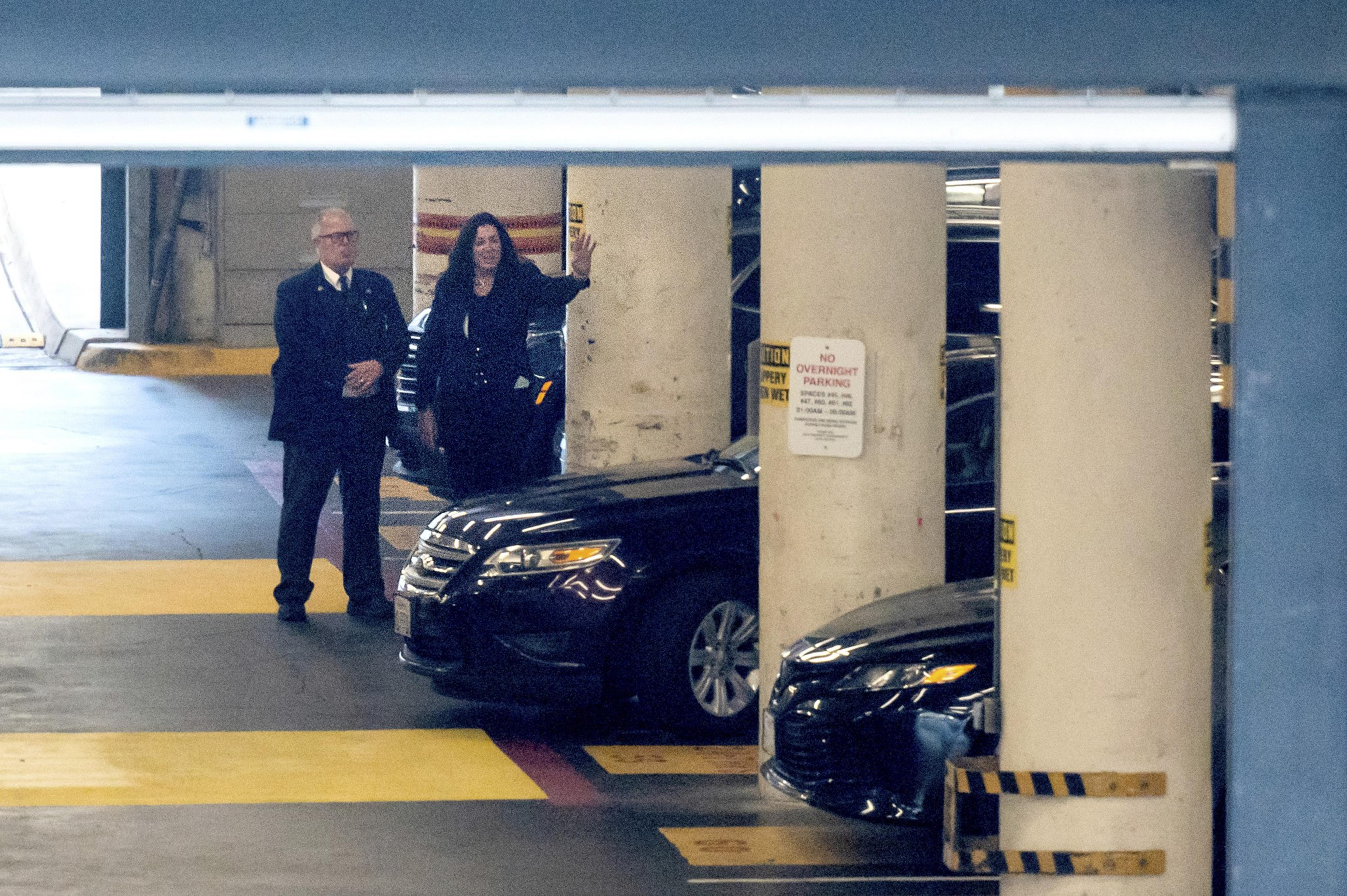 Christine Pelosi walks by two cars in a parking garage beside a man.
