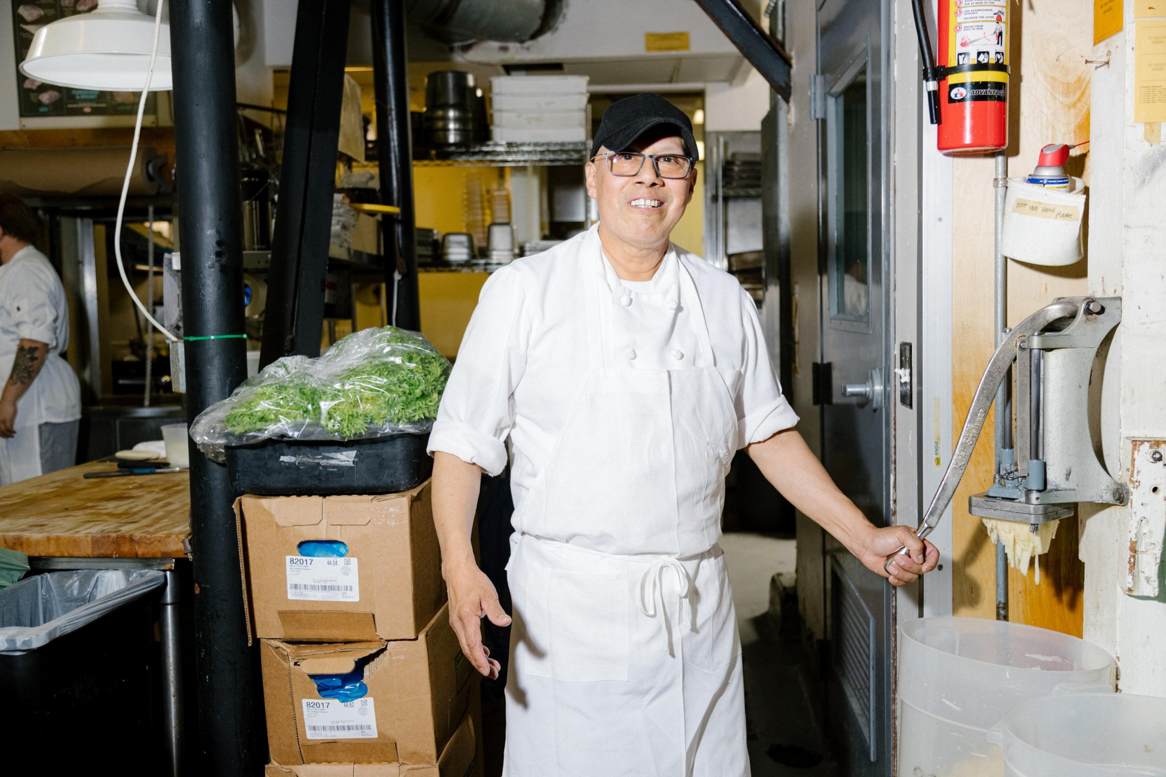 A chef operates a potato press for the shoestring potatoes in a kitchen area.