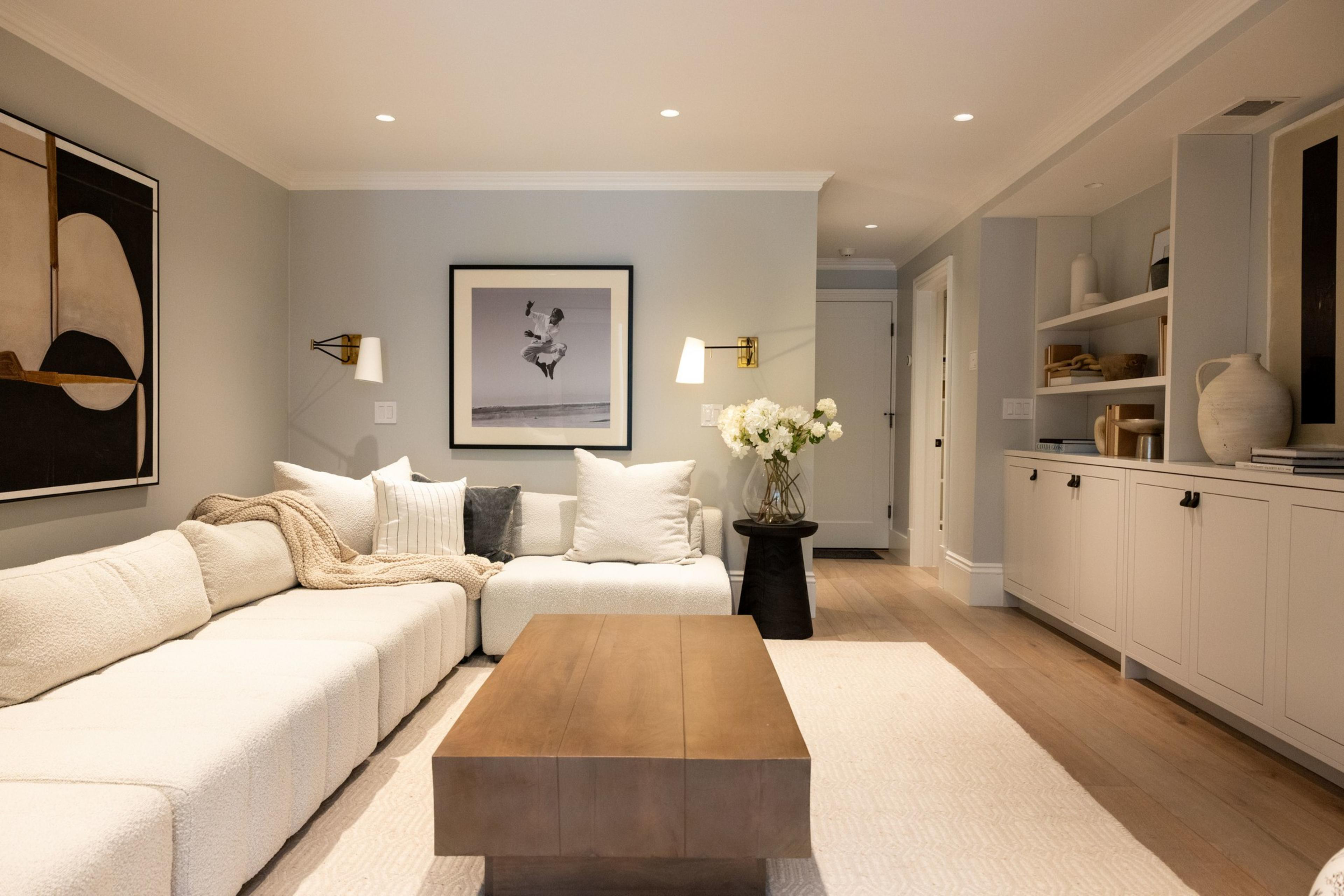 This cozy living room features a white sectional sofa, a wooden coffee table, modern art, a black-and-white photo, built-in shelves with decor, and soft, neutral tones.