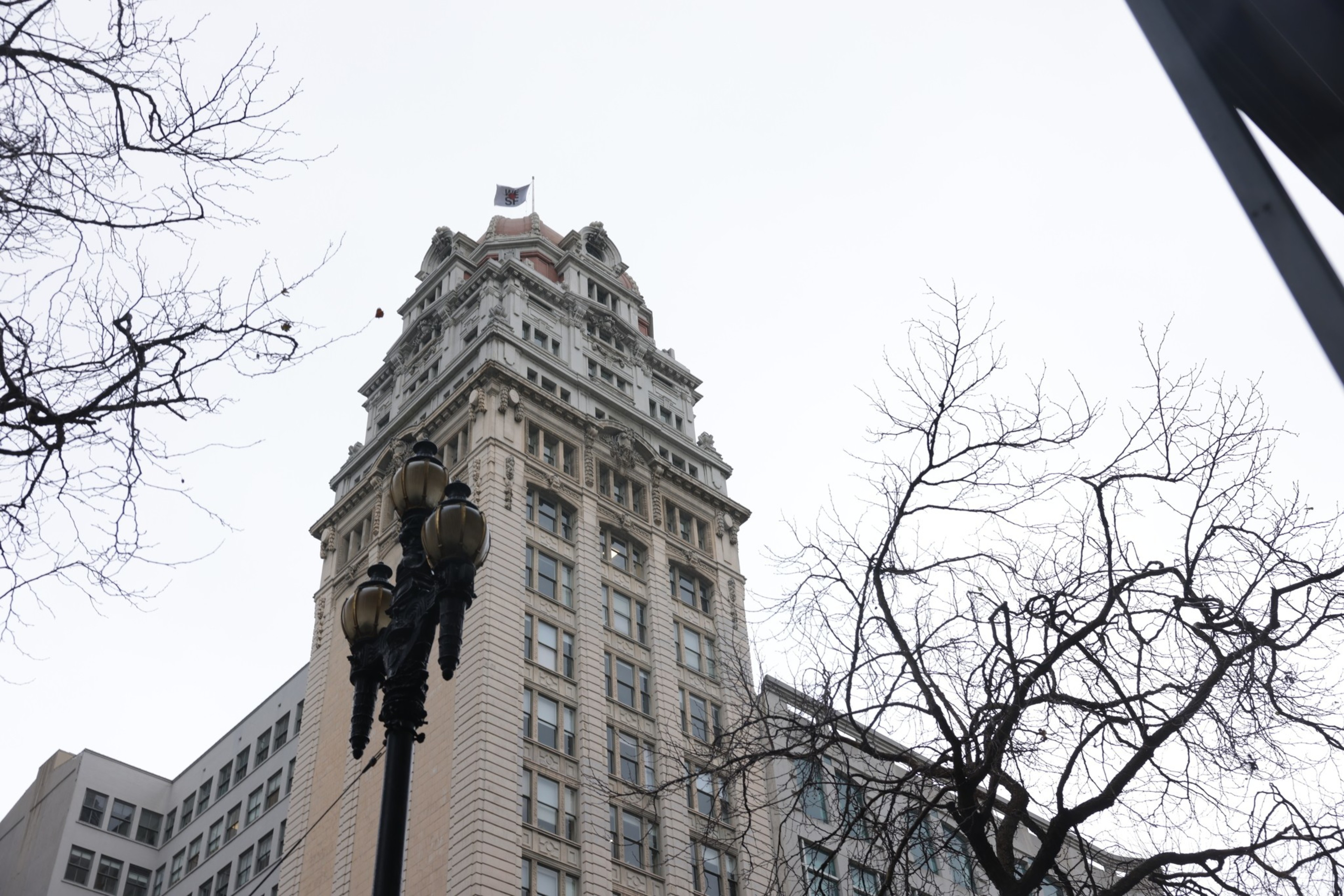 An ornate high-rise building with a street lamp and bare tree branches against a cloudy sky.