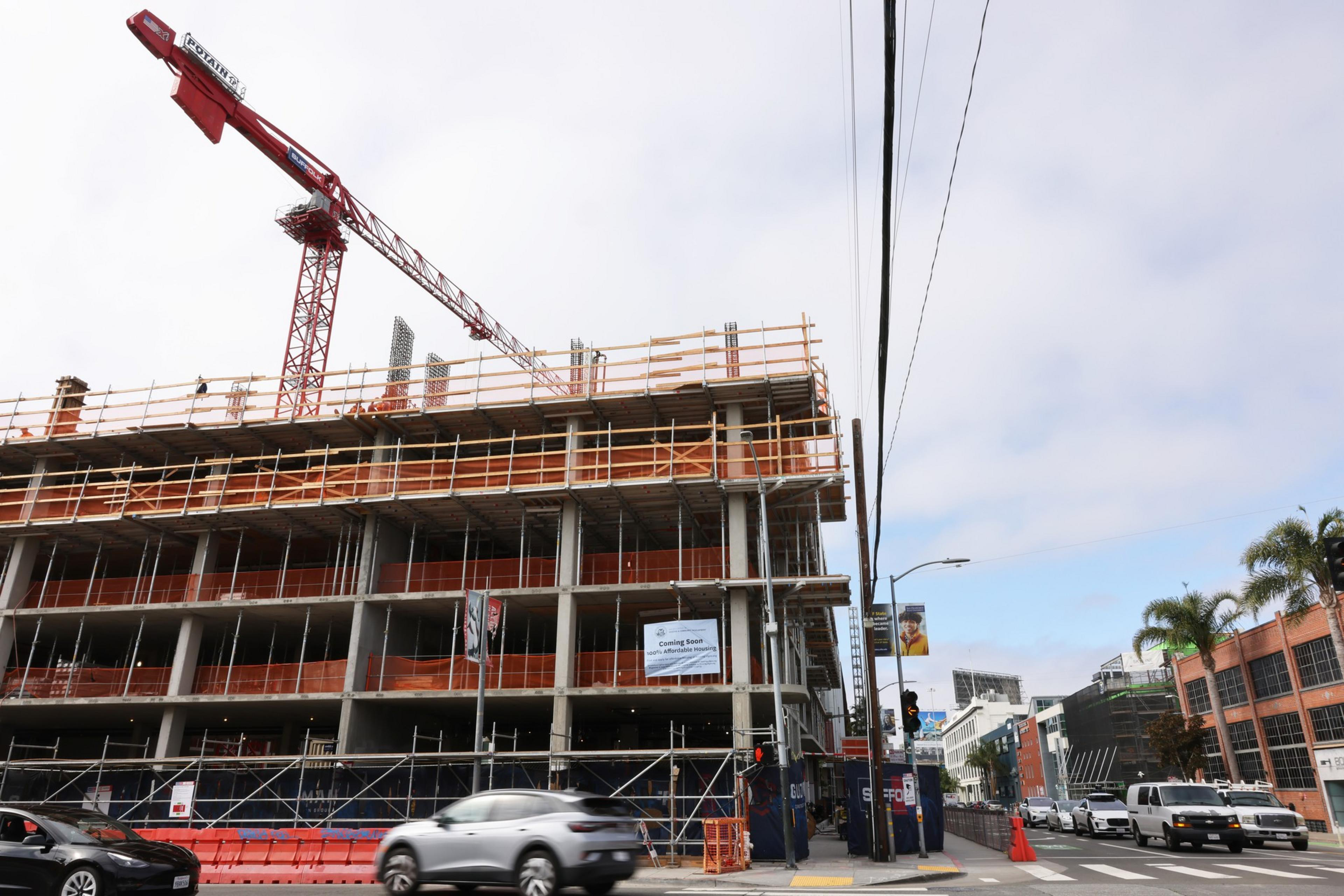 A crane rises above a multistory building under construction as a car drives by