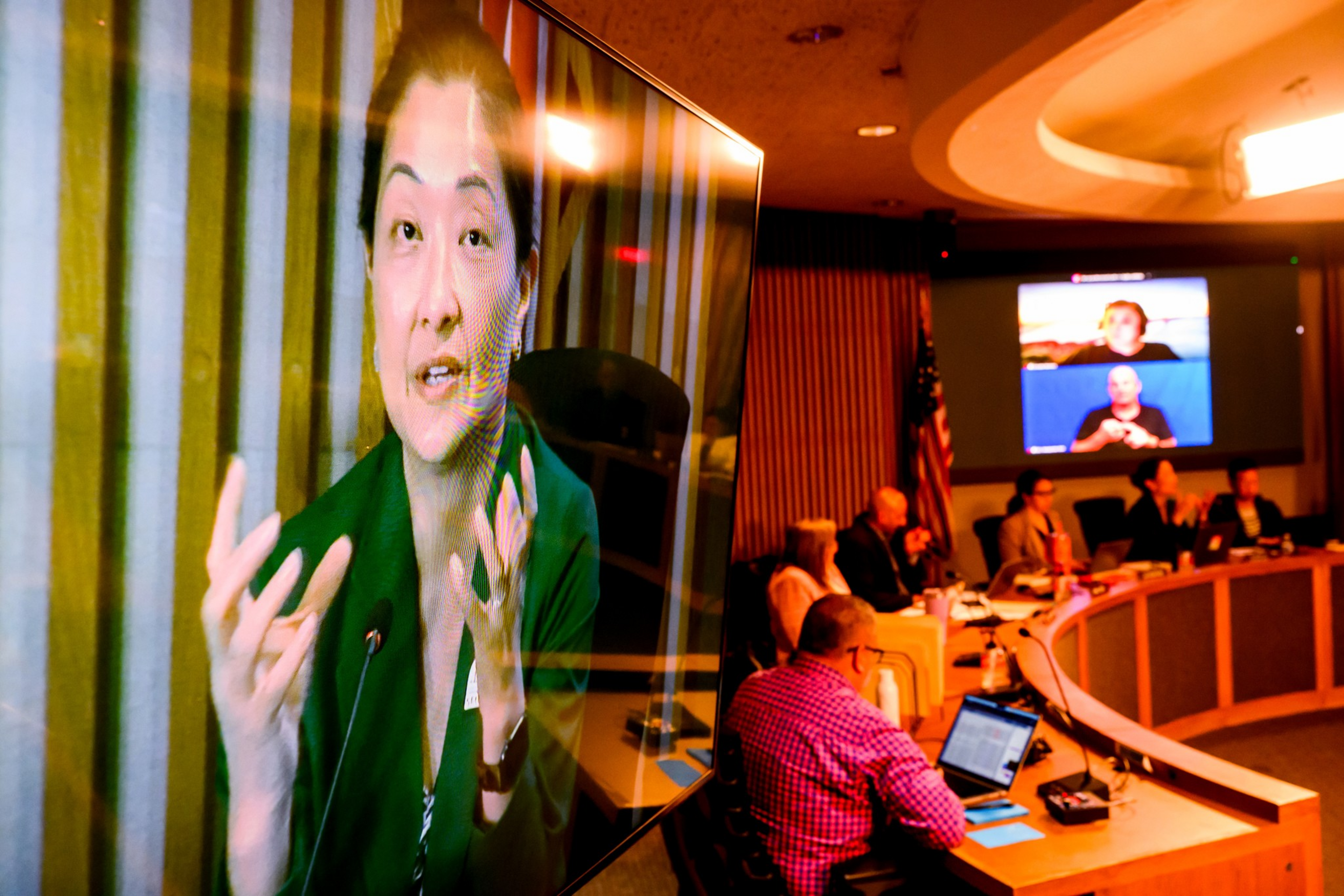 A woman speaks on a large screen during a meeting with several people ...