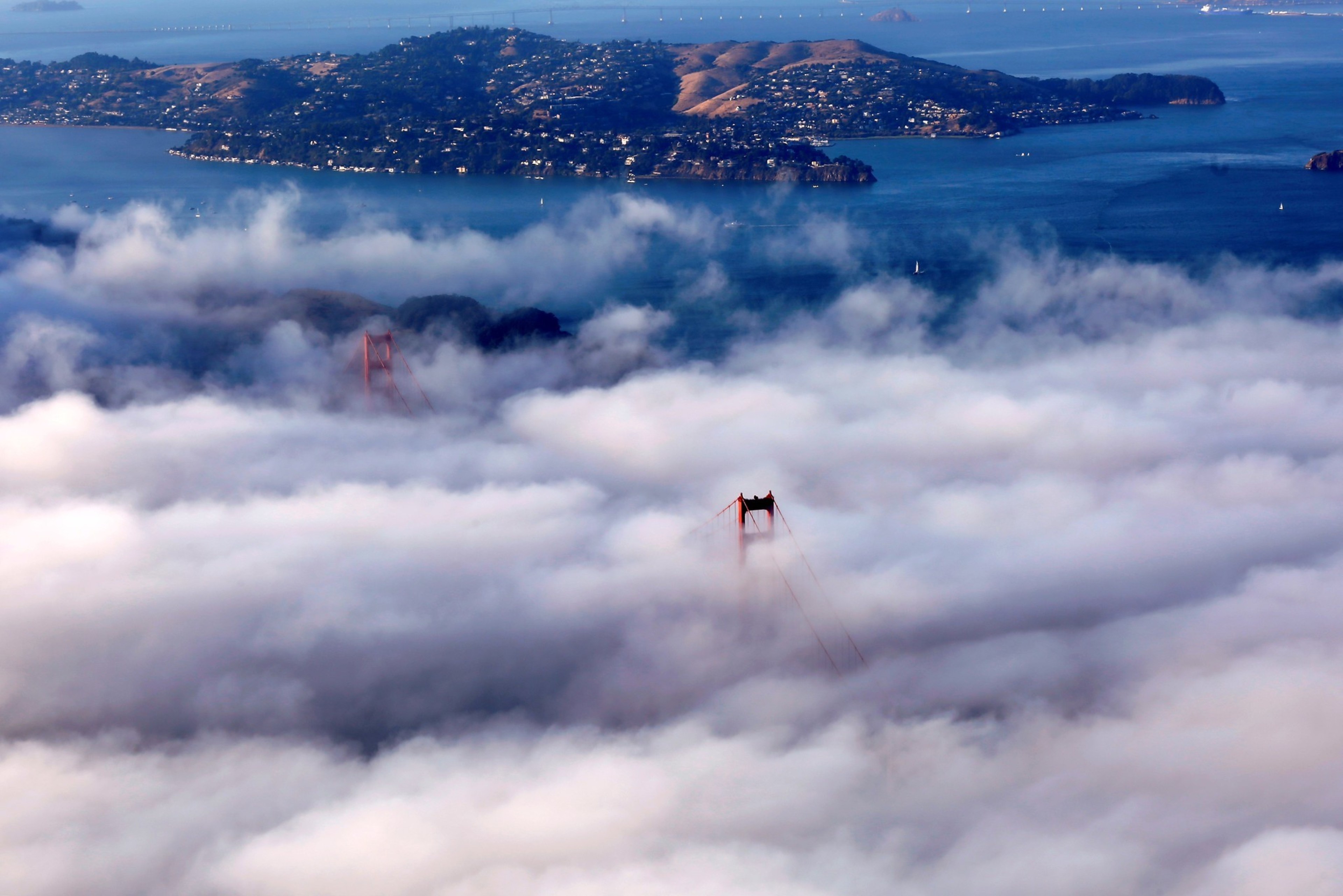 The image shows the Golden Gate Bridge towers peeking through thick fog, with a distant hilly island and ocean forming the scenic background.