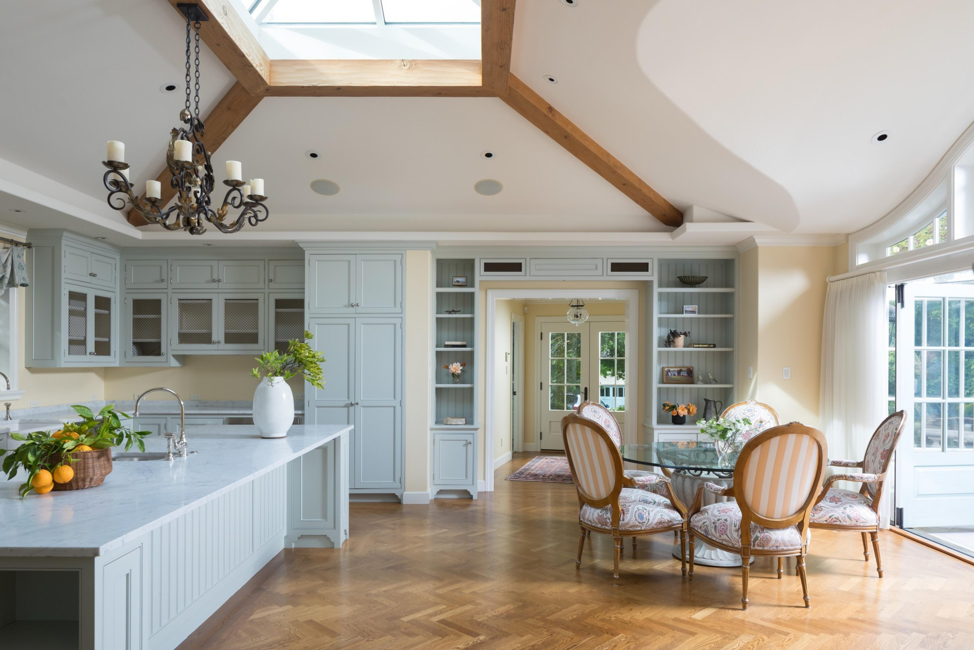 A bright, spacious kitchen with wooden floors, light blue cabinets, and a dining area with a glass table and upholstered chairs.