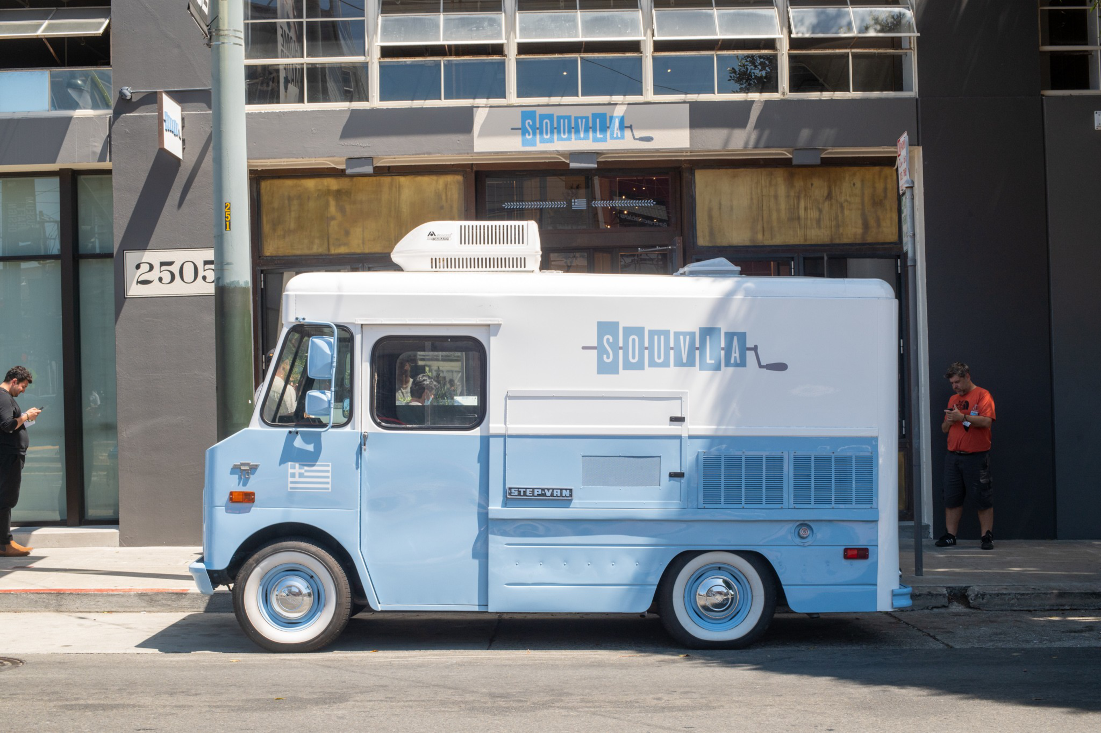 A light blue and white vintage food truck labeled "souvla" is parked on a city street in front of a building numbered 2505.