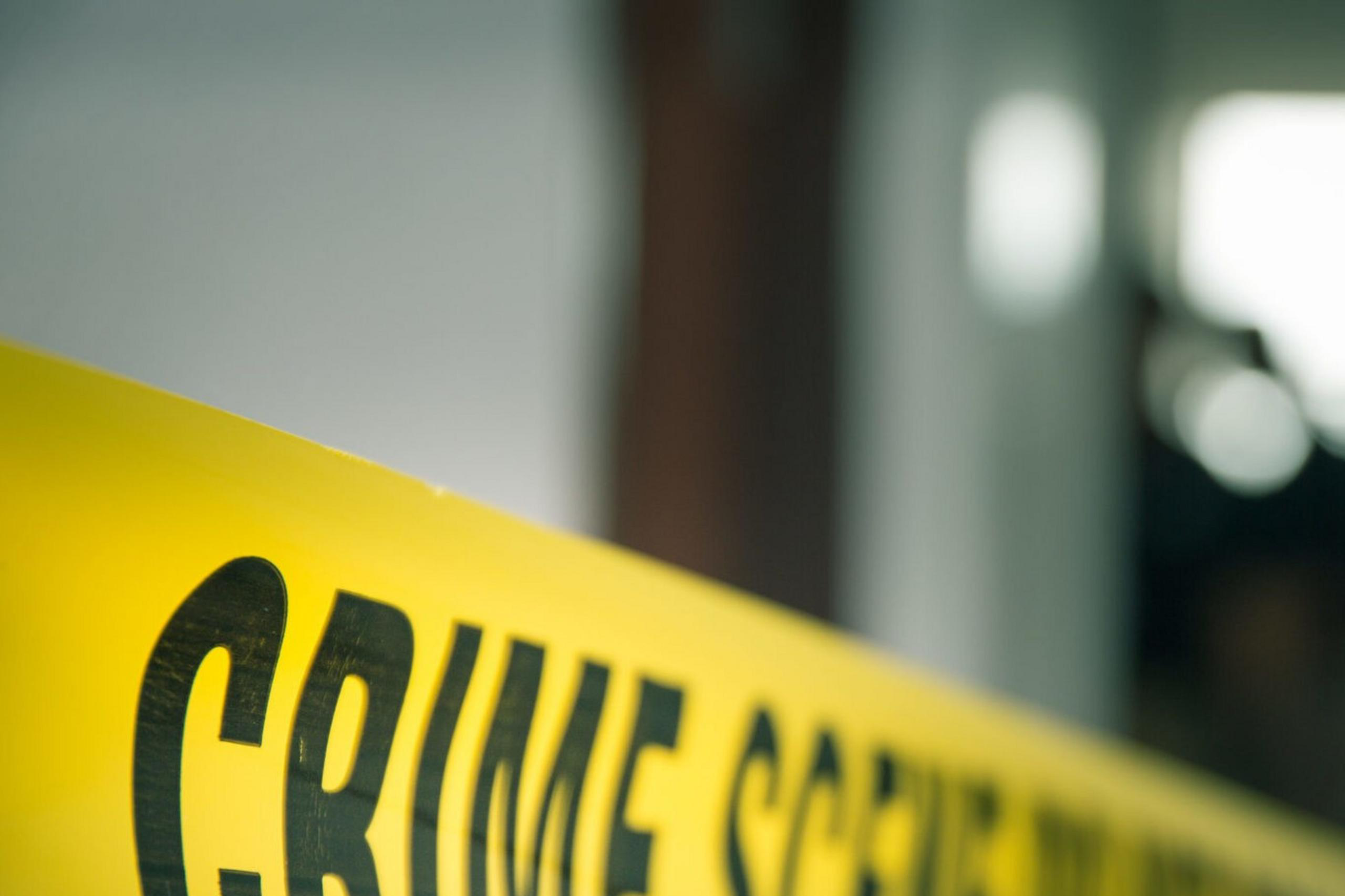 Crime scene police tape is visible across an image with shadowy figures in an interior doorway.