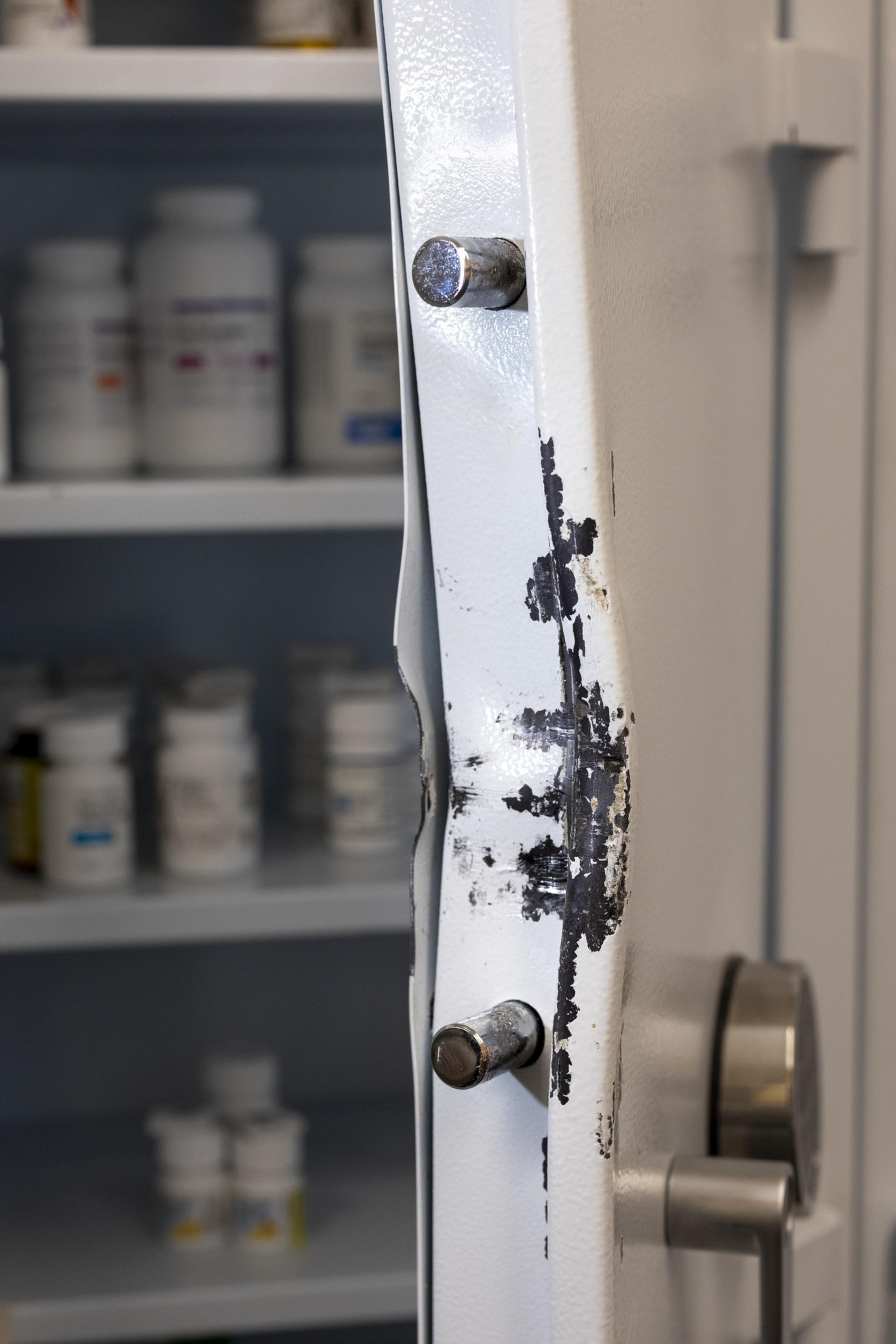 A safe door with chipped paint is slightly ajar, revealing shelves filled with various medicine bottles inside.