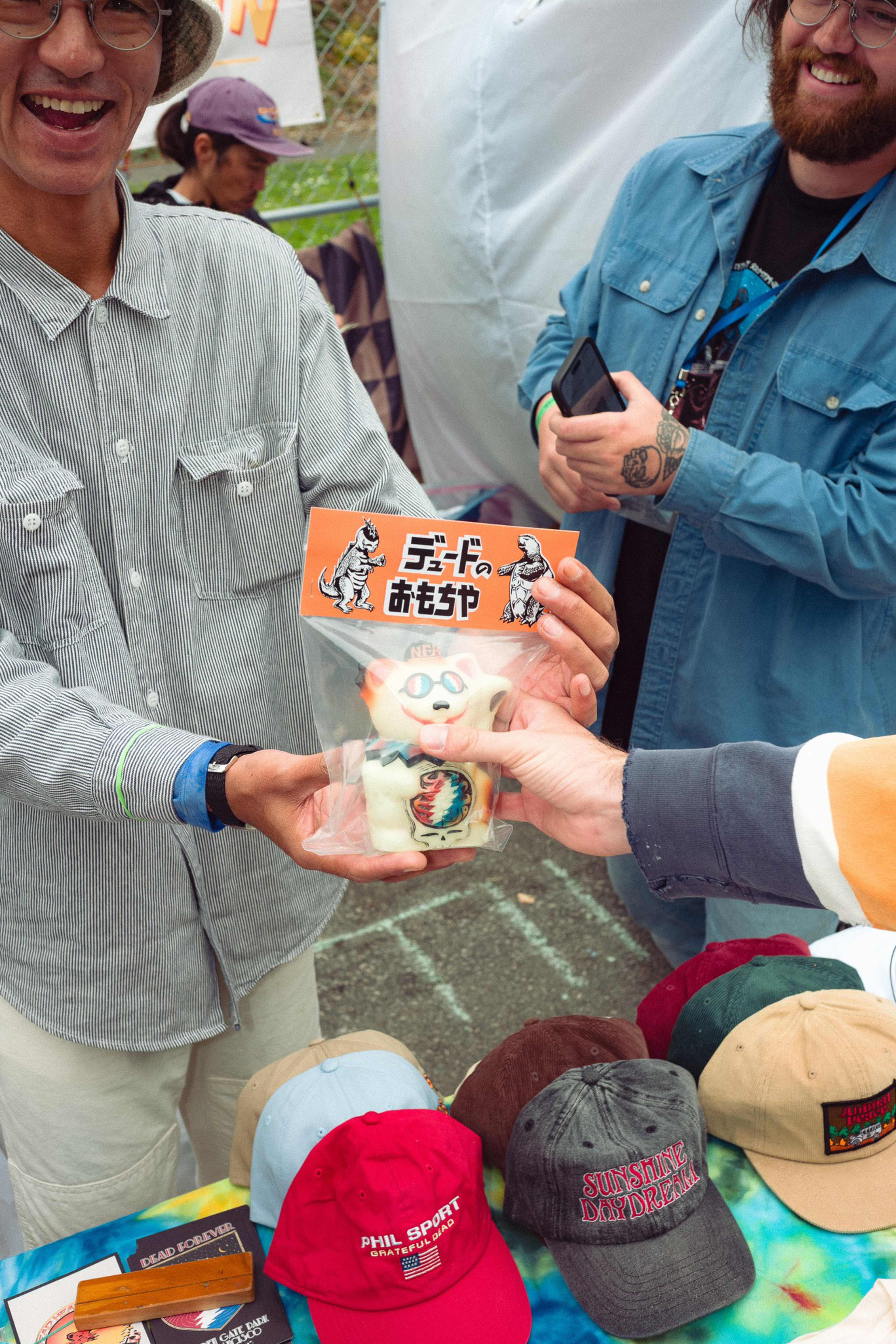 A person holds up a packaged toy with Japanese text, while others around a table display various colorful caps and smile.
