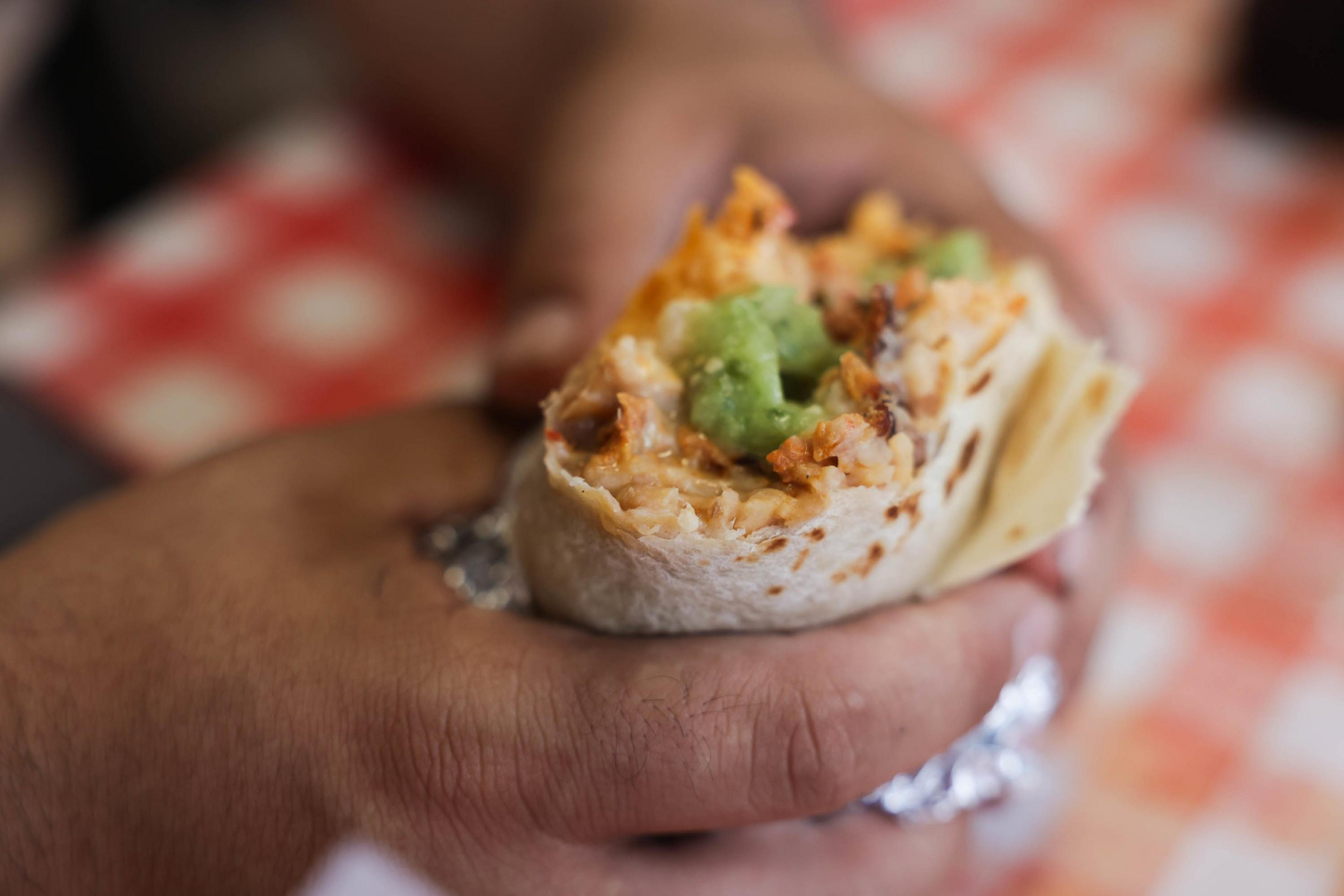 A half-eaten burrito with fillings visible, held in a hand over a checkered tablecloth.
