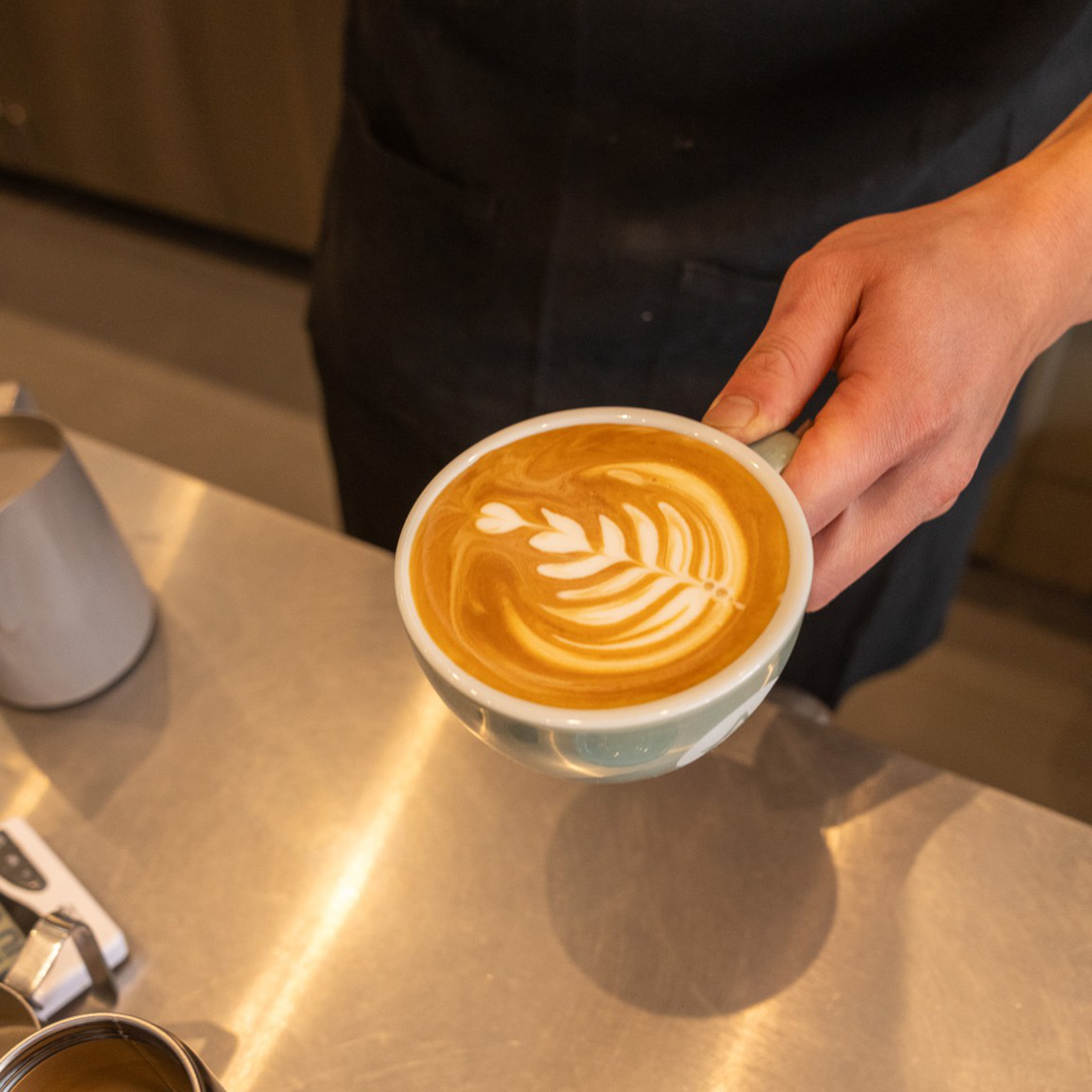 A hand holds a cappuccino, with a lovely design. 