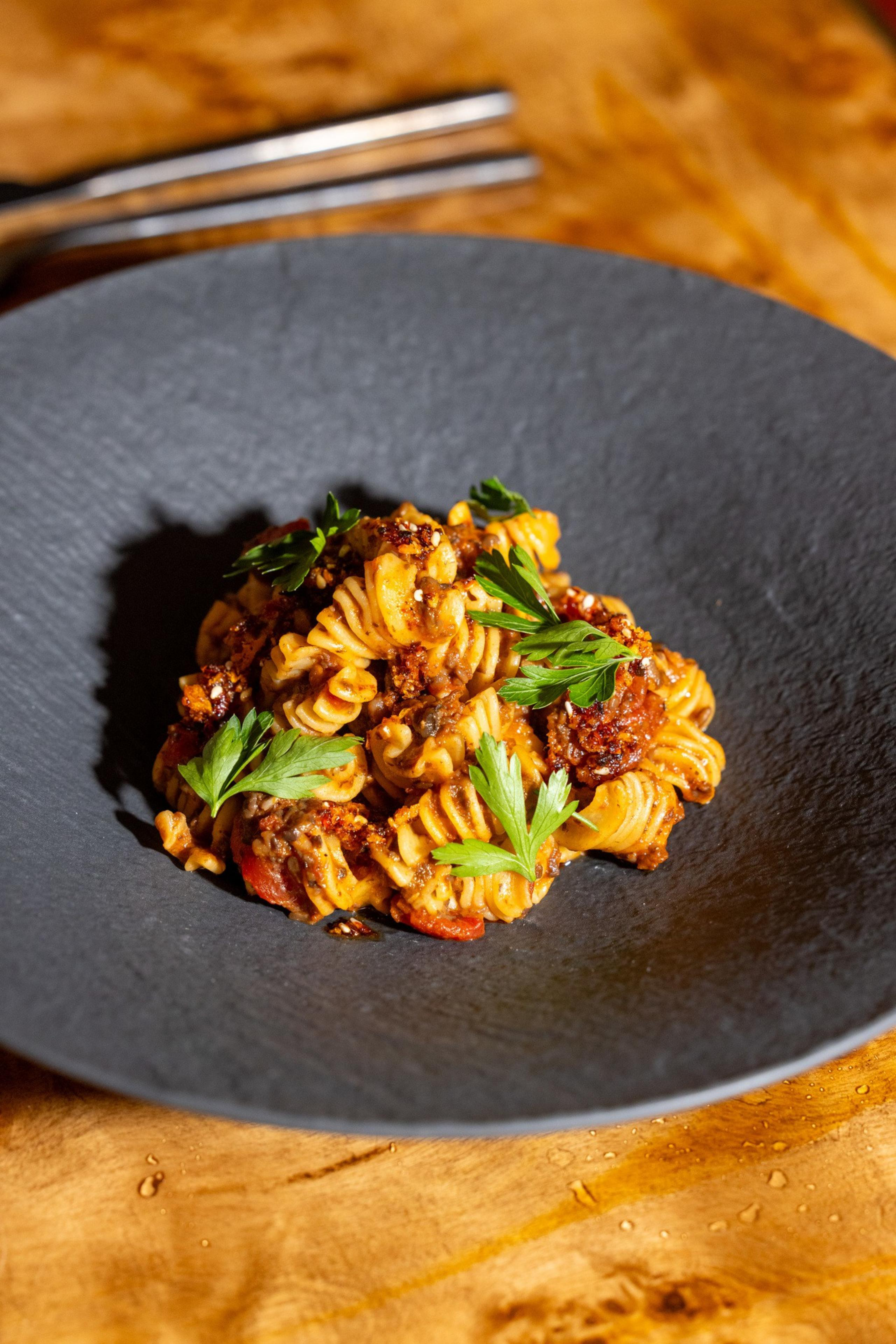 Spiral pasta in a rich tomato sauce with ground meat, garnished with fresh green parsley leaves, served on a black textured plate.