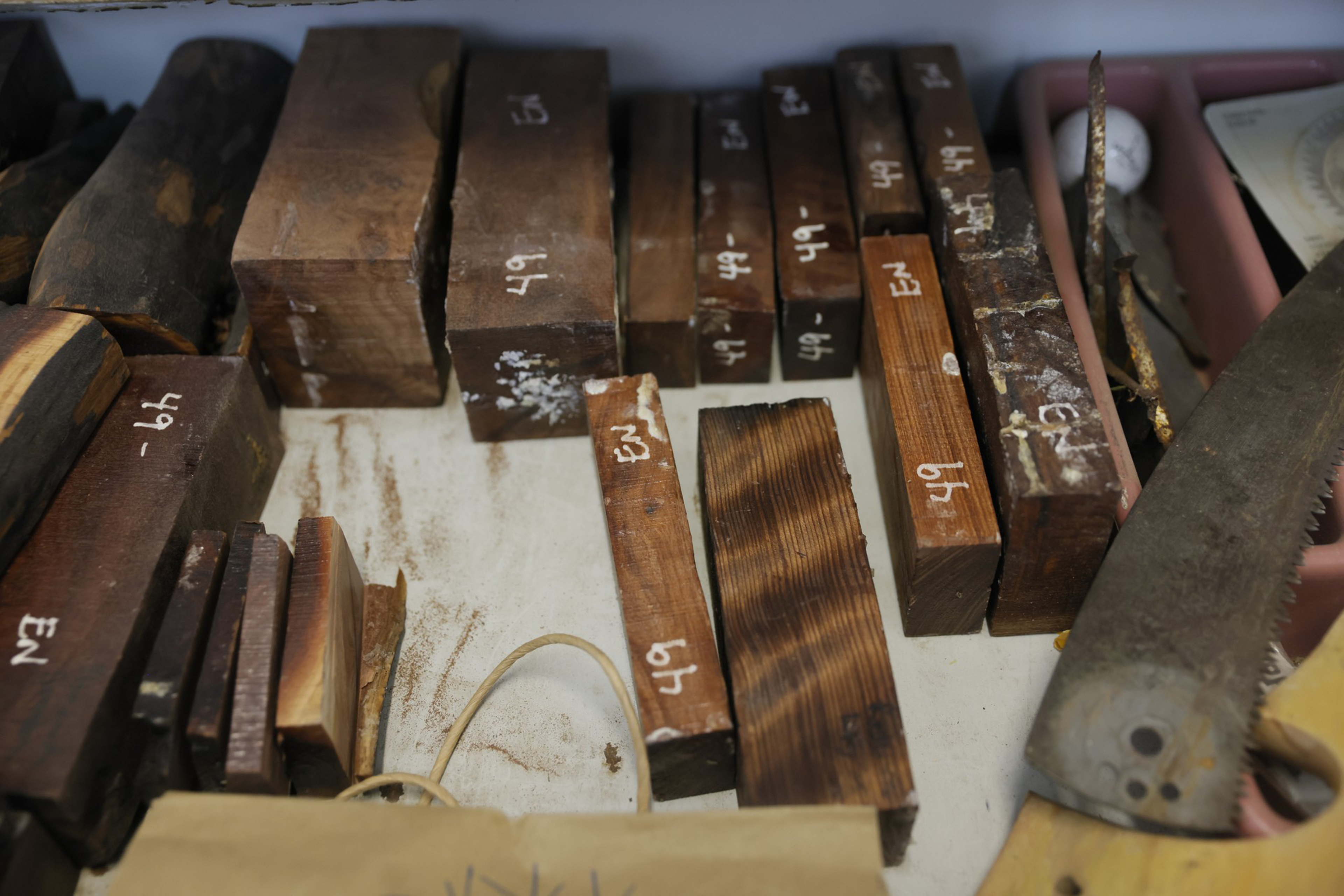 Several small wooden blocks labeled “49” and “EN” are arranged on a surface next to a saw blade and rubber band.