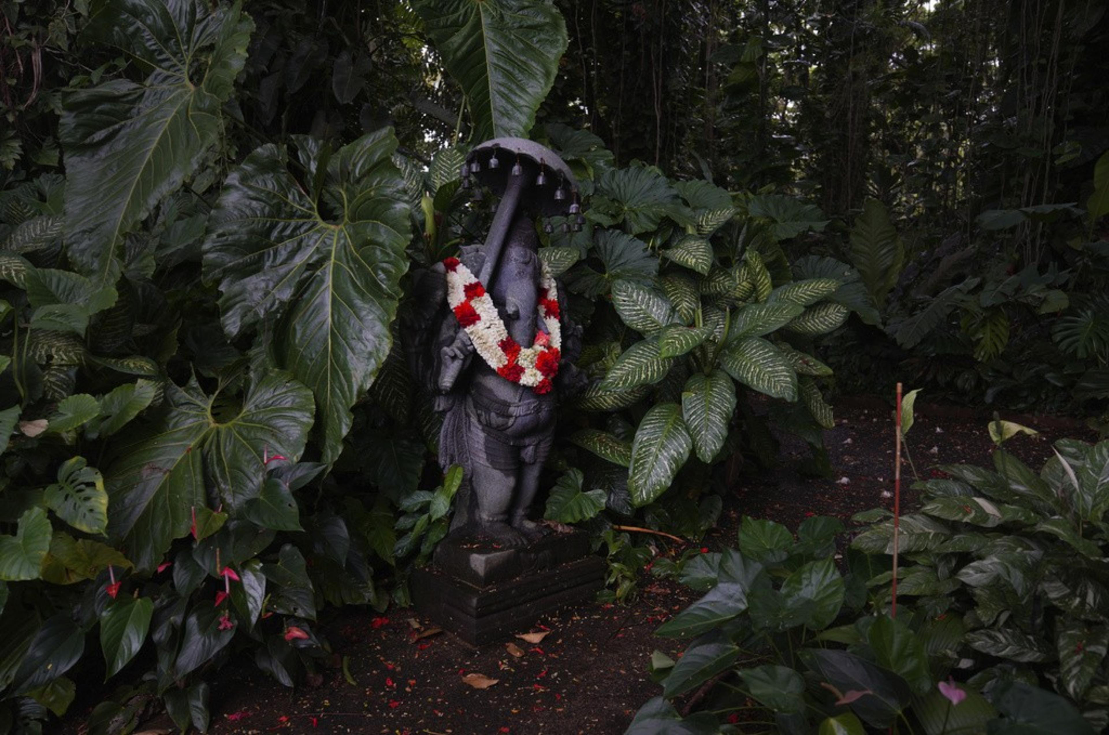 A gray statue of an elephant god stands in a lush forest.