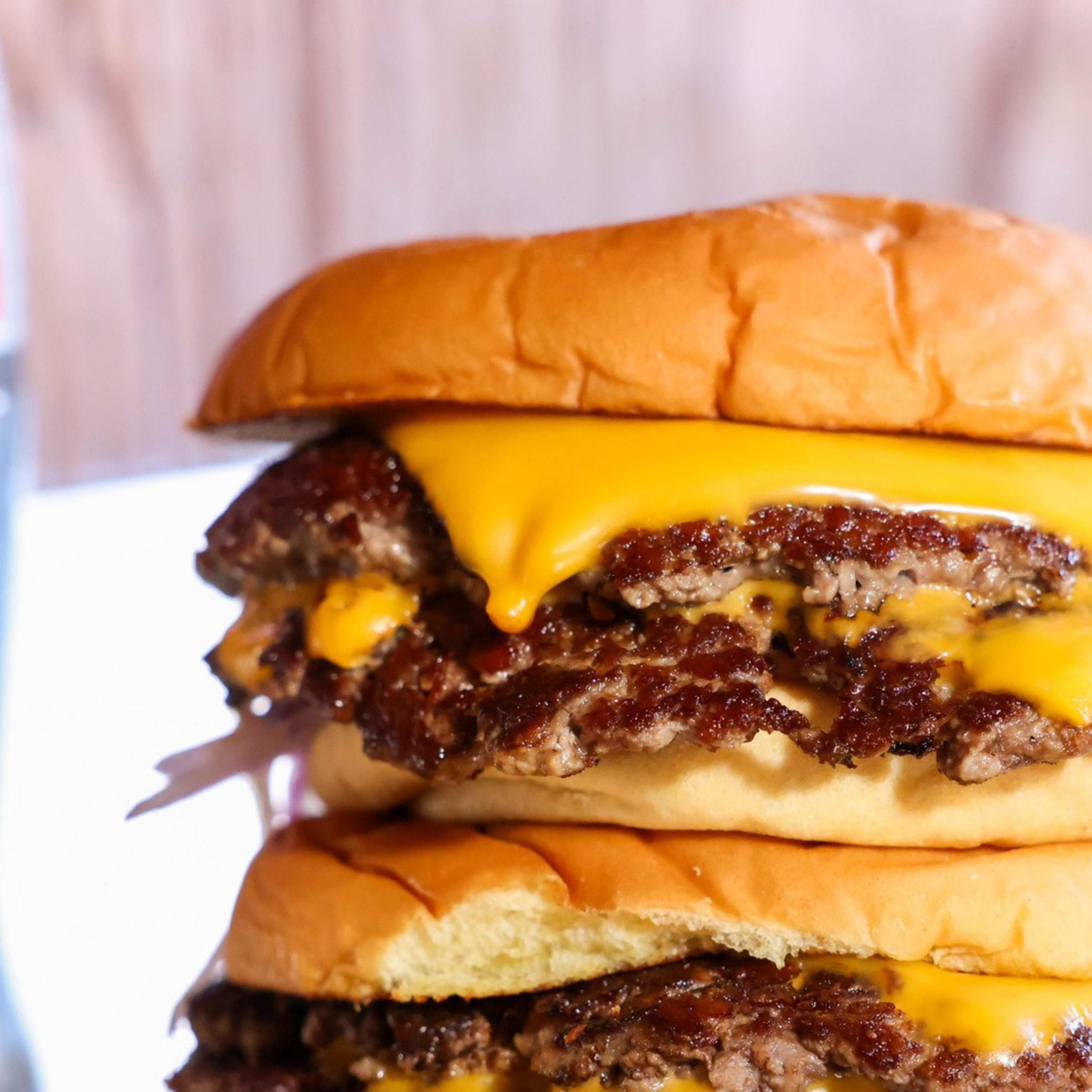 A double cheeseburger with melted cheese and beef patties is stacked high, accompanied by bottles of Coke and beer in the background.