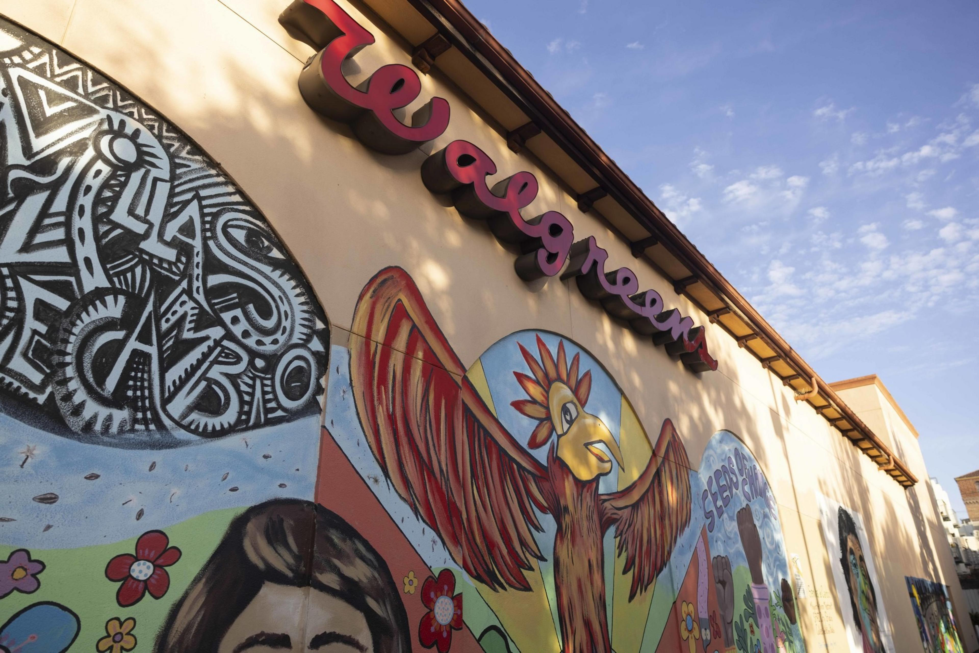 A colorful mural on a store wall features a bird with outstretched wings, floral designs, and bold text under a &quot;Walgreens&quot; sign.
