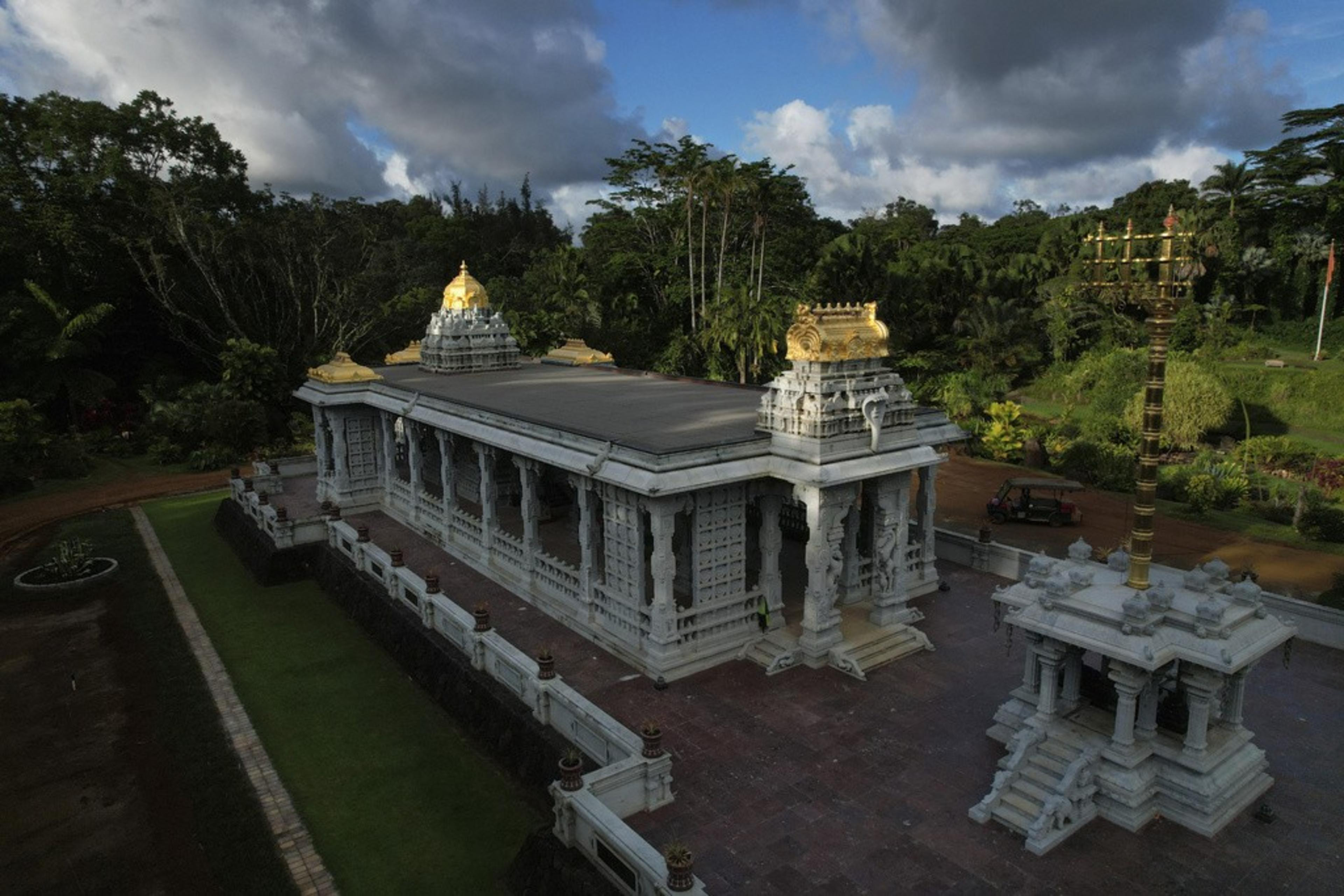 A white temple made of granite and topped with gold decorations sits in a tropical clearing.