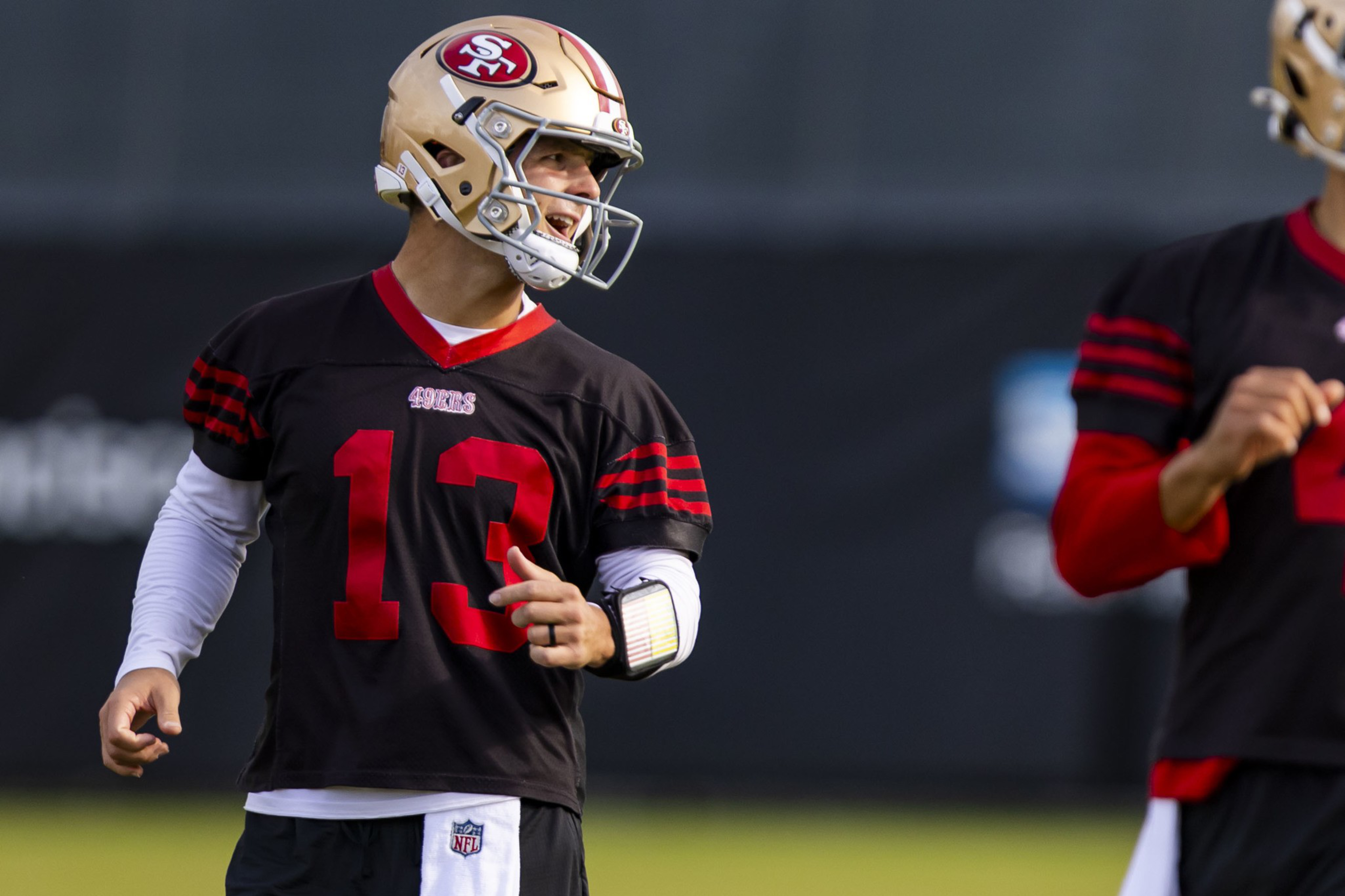 A football player wearing a San Francisco 49ers helmet and black jersey with number 13 gestures while looking to his left.