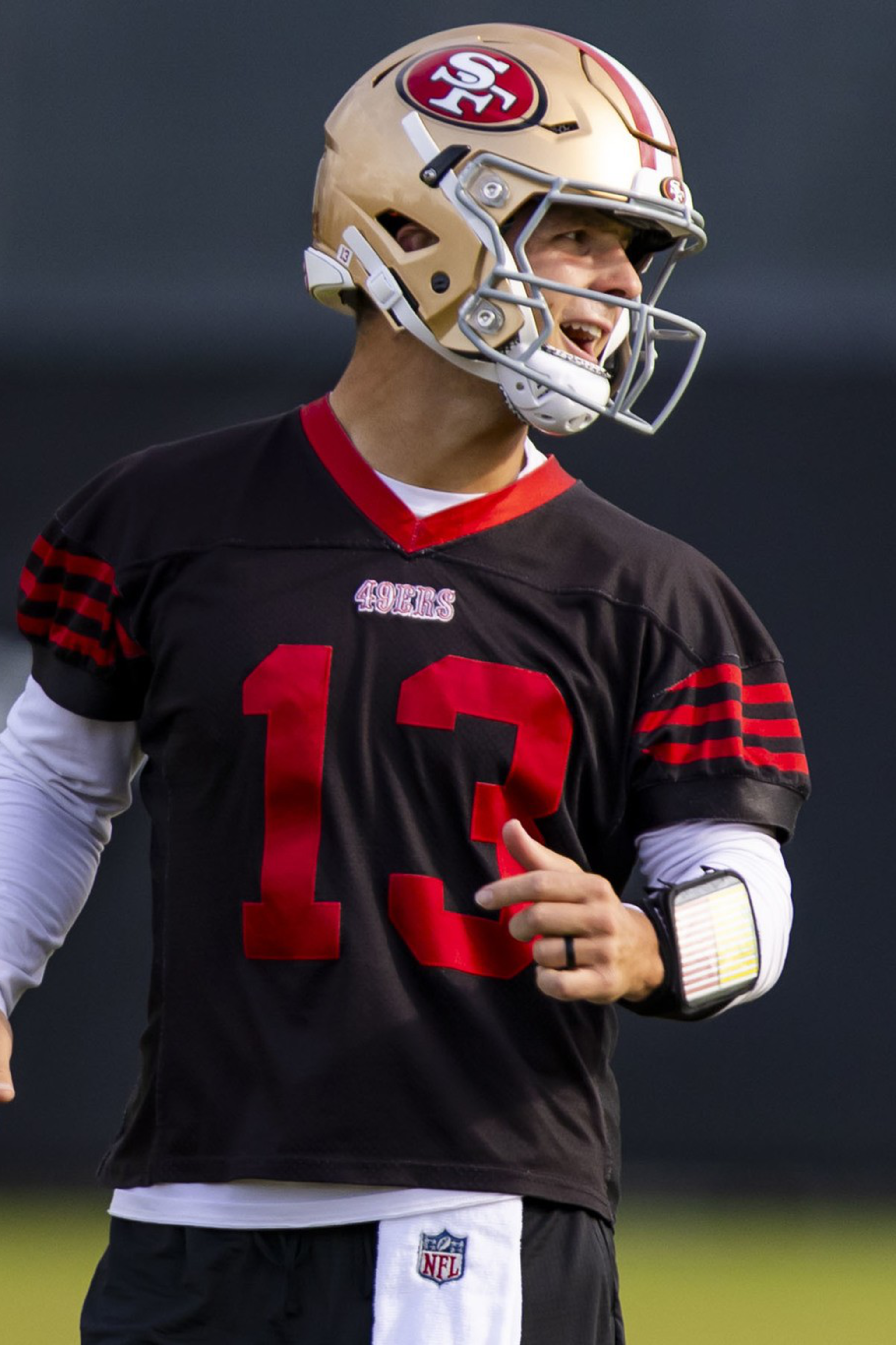 A football player wearing a San Francisco 49ers helmet and black jersey with number 13 gestures while looking to his left.