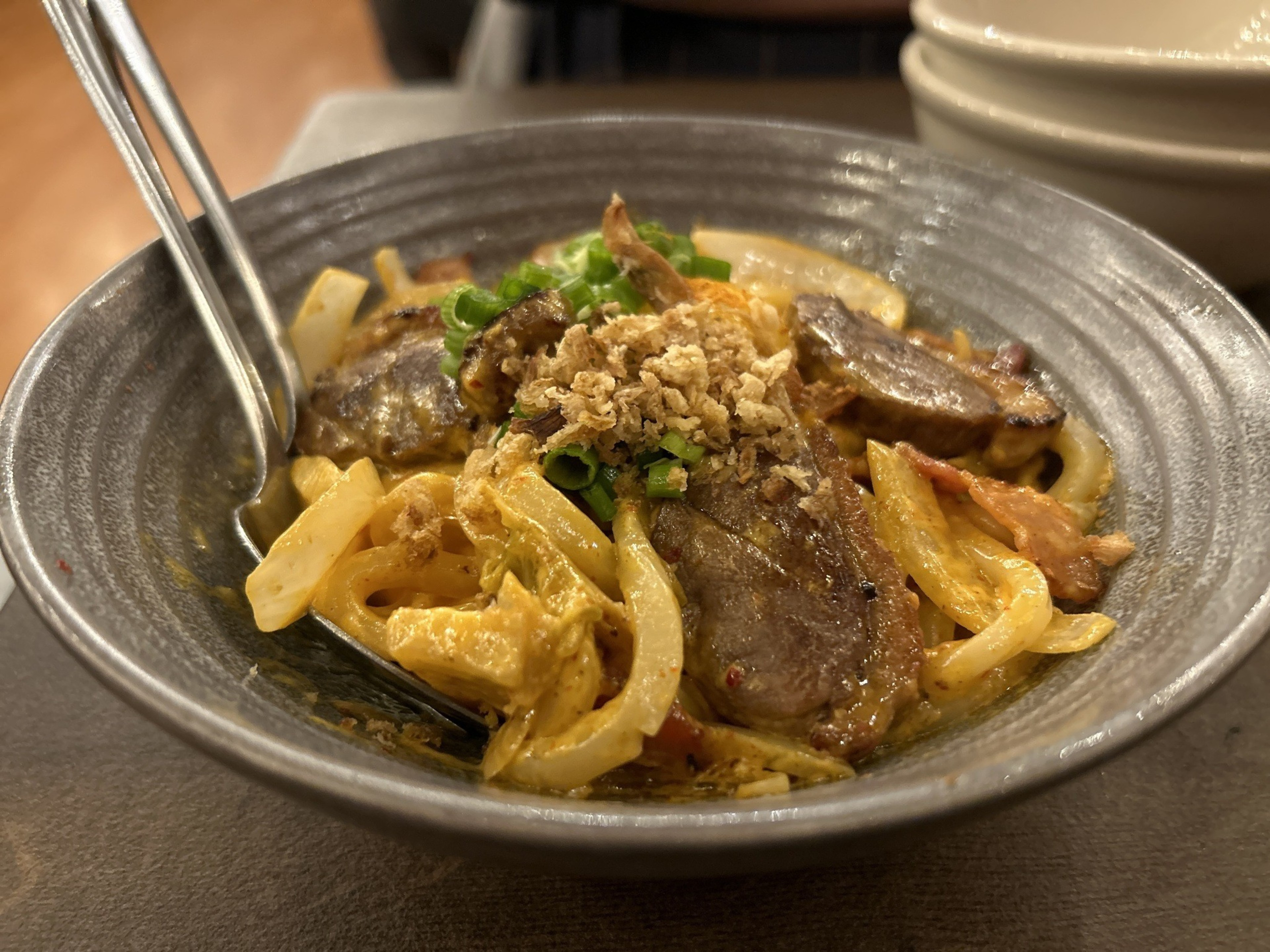 a ceramic bowl of udon carbonara with a serving spoon poking out