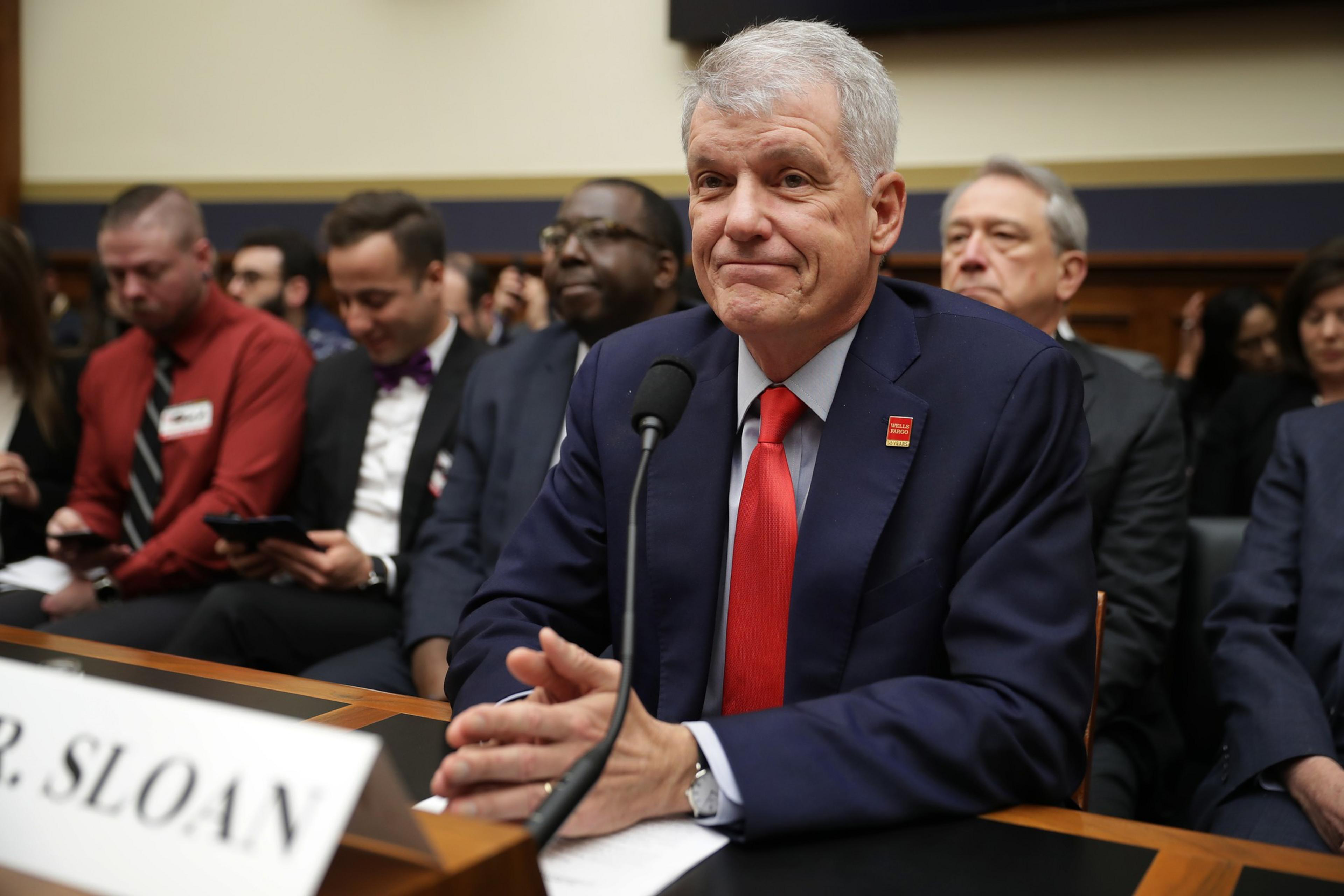 A man in a suit with a red tie is about to speak in front of a mike.