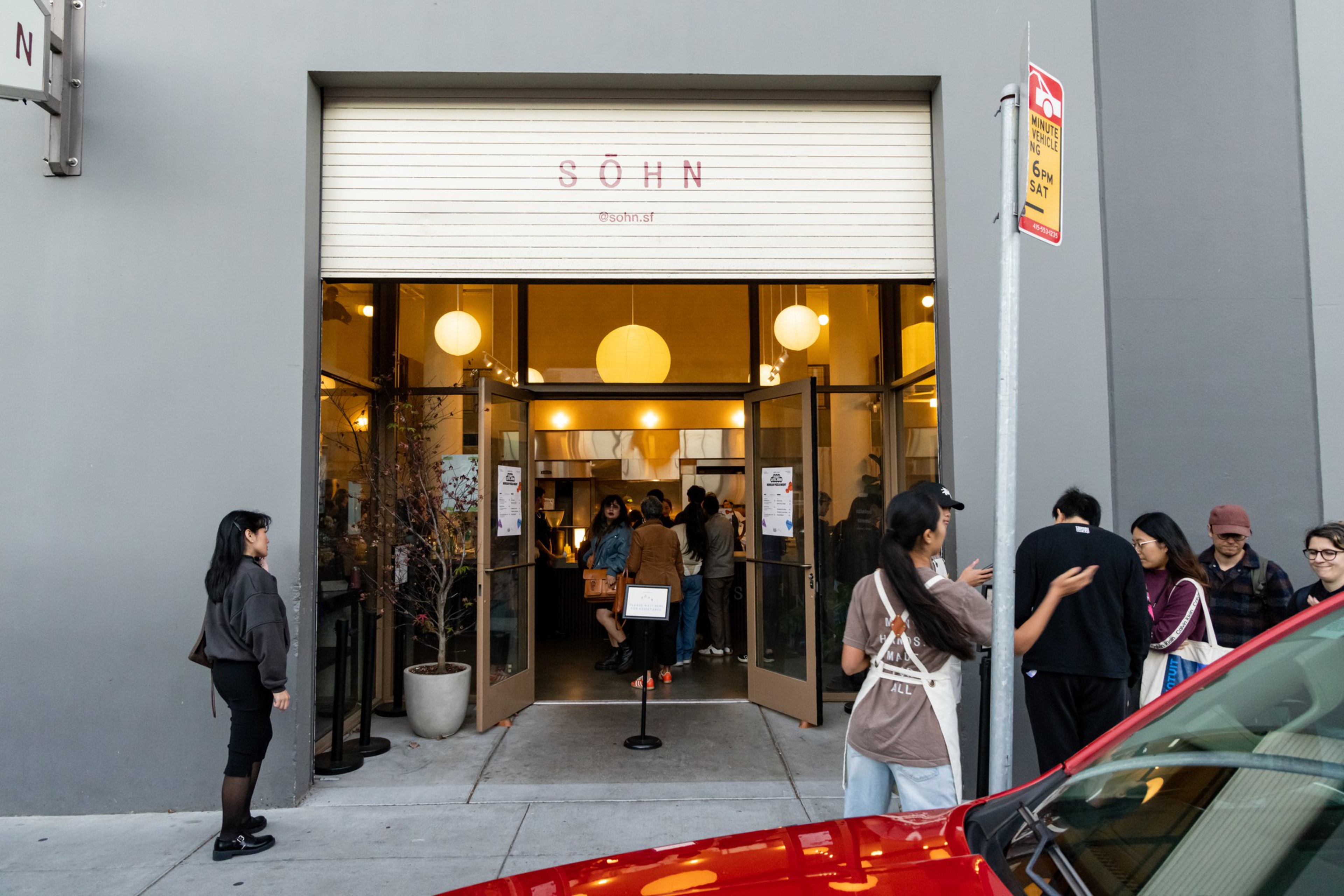 People are gathered outside and inside a warmly lit cafe called SÖHN, with open double doors and a sign displaying the cafe'sInstagram handle.