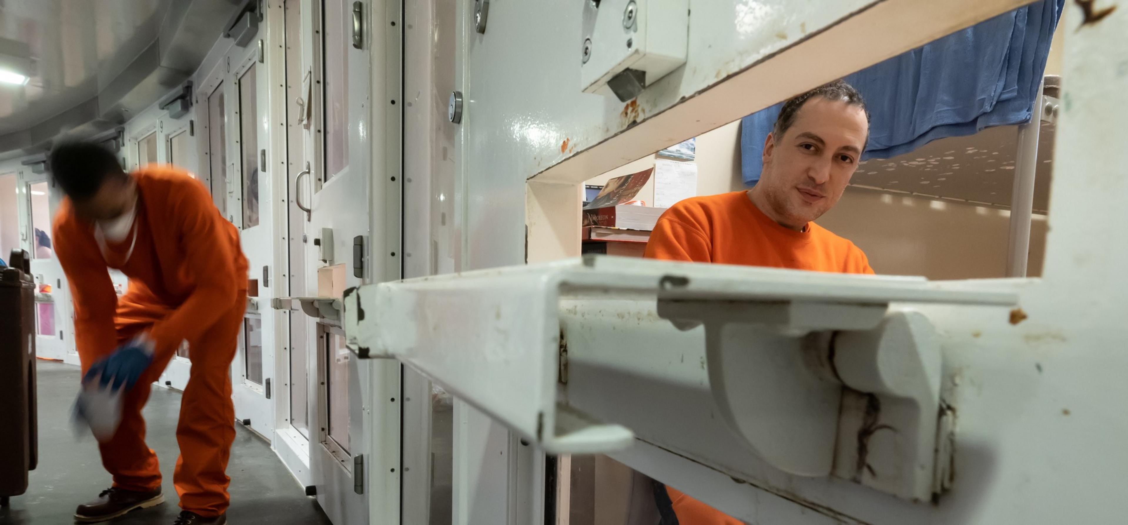 Jail inmate Nima Momeni, suspect for the killing of Cash App founder Bob Lee, while dressed in an orange sweatshirt and sweatpants looks out the slot in his cell door at the San Jail with another inmate in the background.