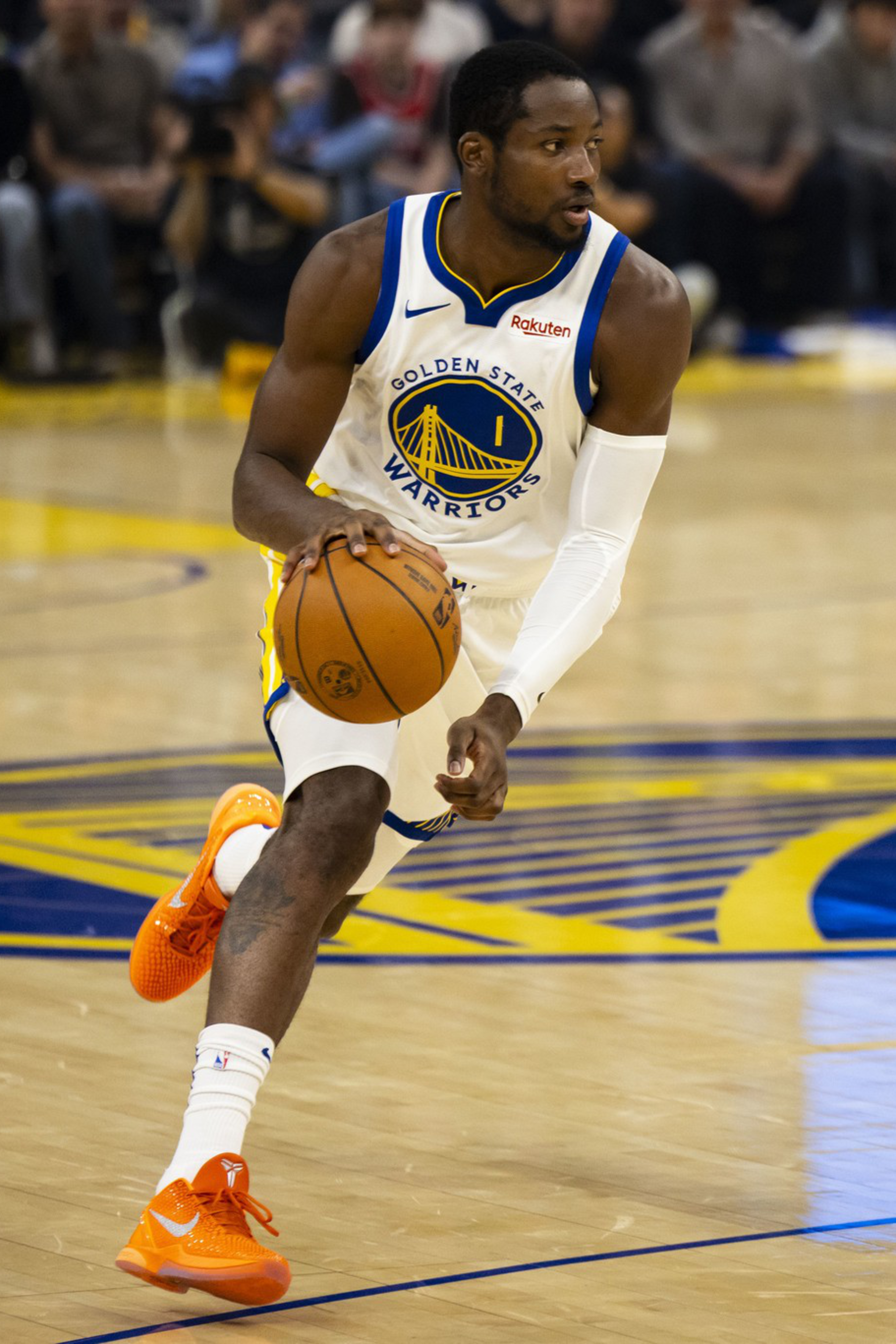 A Golden State Warriors player dribbles the basketball while being closely guarded by an opponent wearing a navy blue jersey with the number 5.