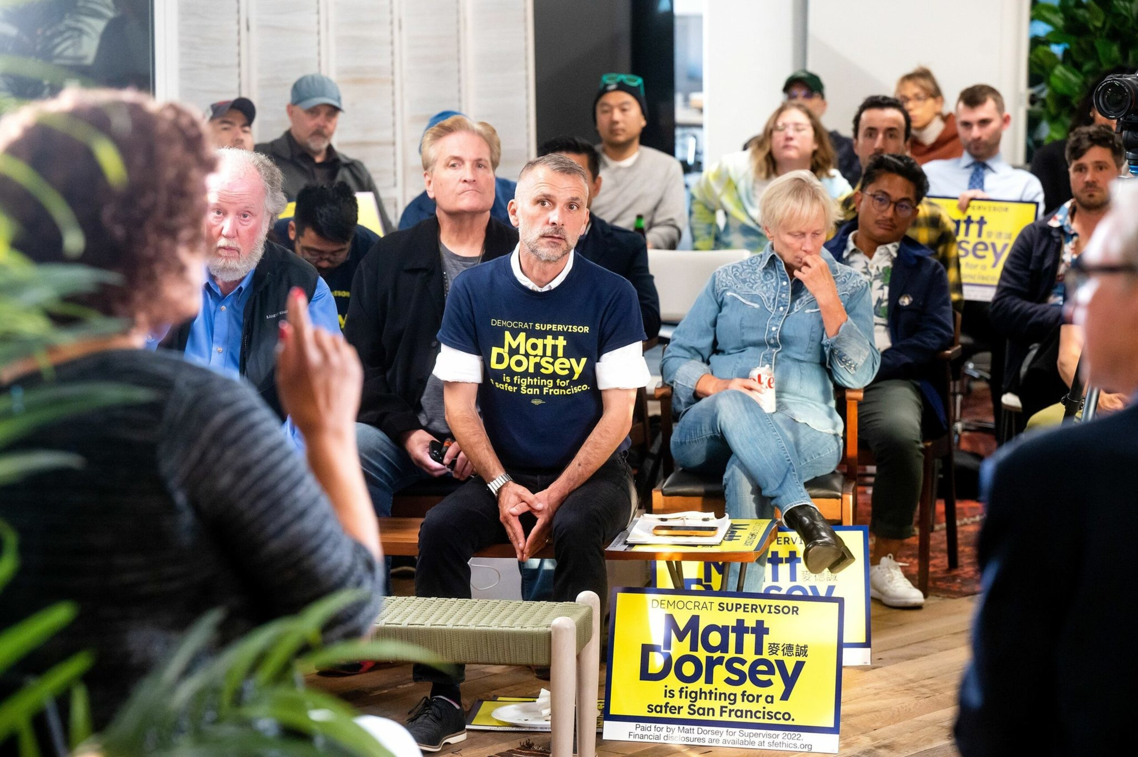 A diverse group of people attentively listens during a political event, with several holding signs supporting Matt Dorsey for San Francisco supervisor.