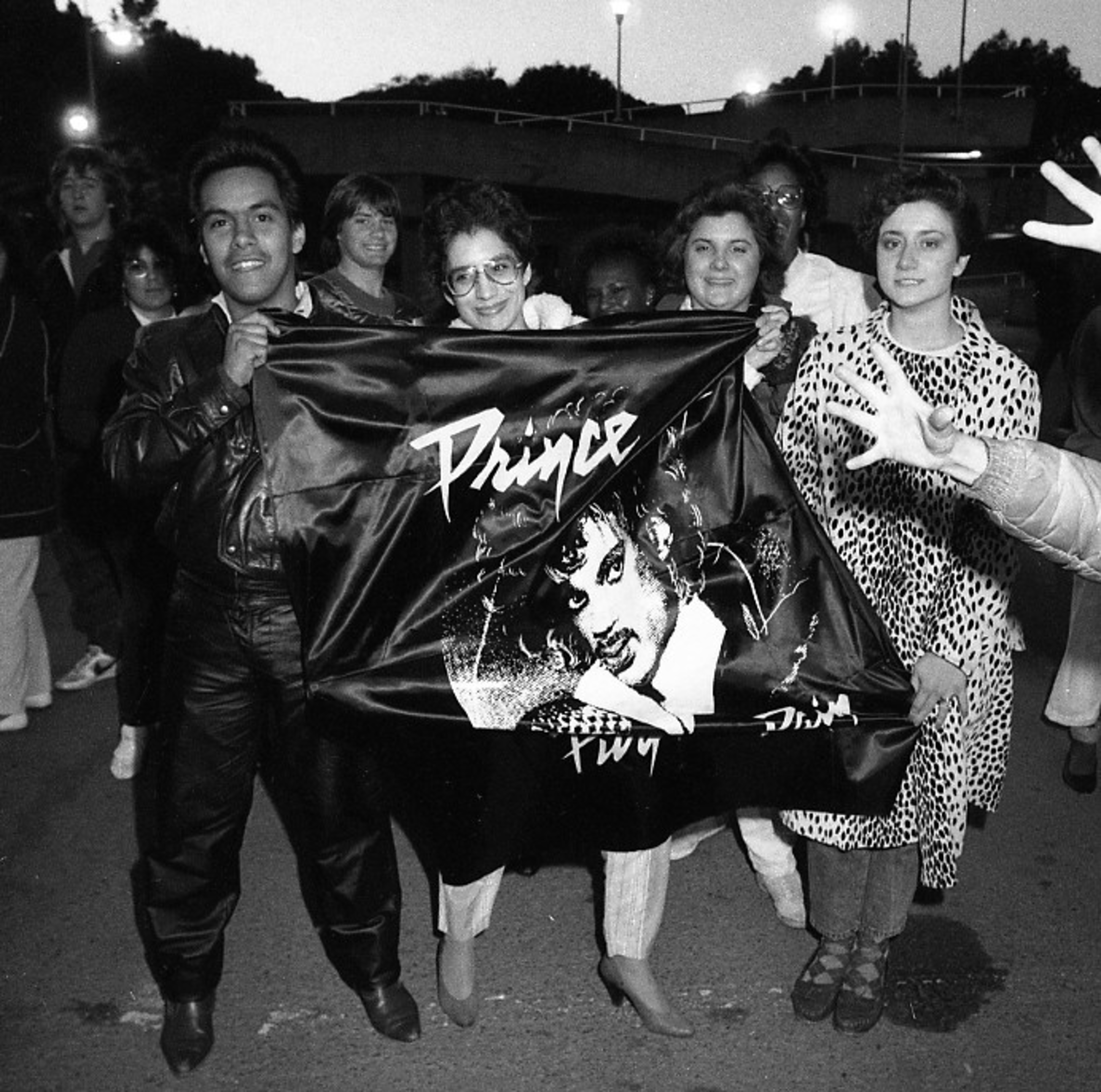 A group of fans holds up a banner with an image of the musician Prince.
