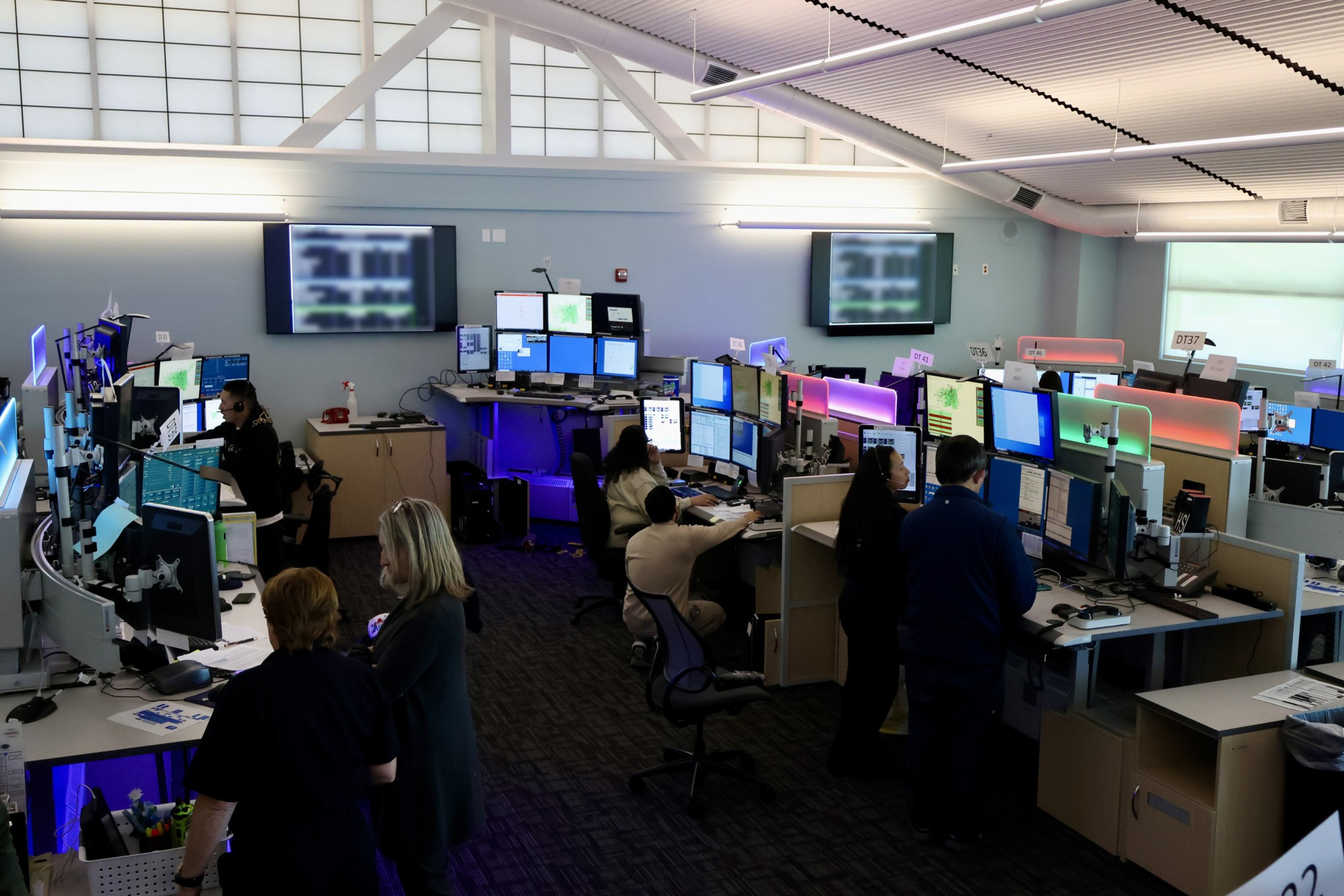 An office with workers at computers, multiple screens, and TVs on walls.