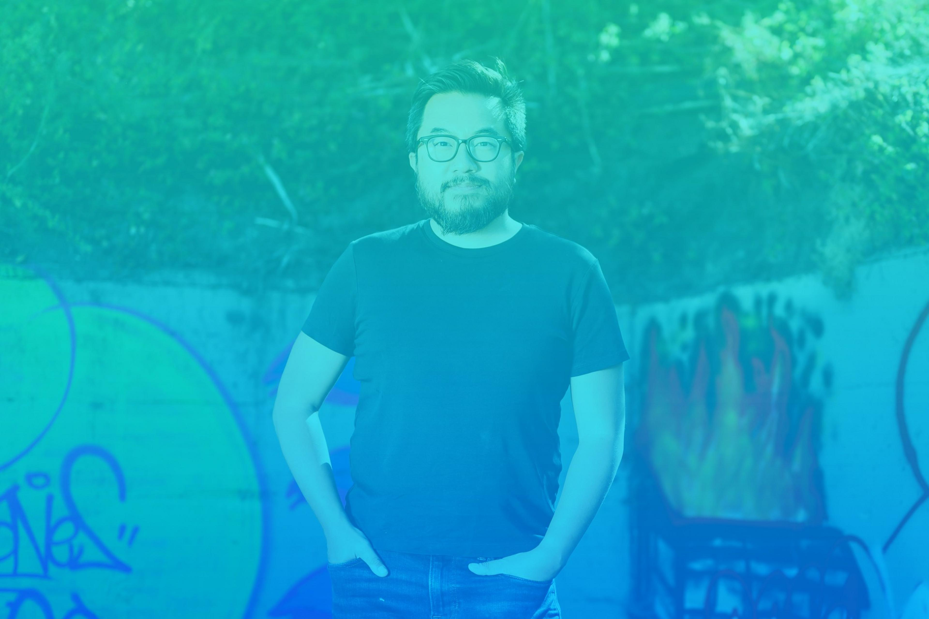 A man stands in front of graffiti-covered walls, with a blue color overlay.