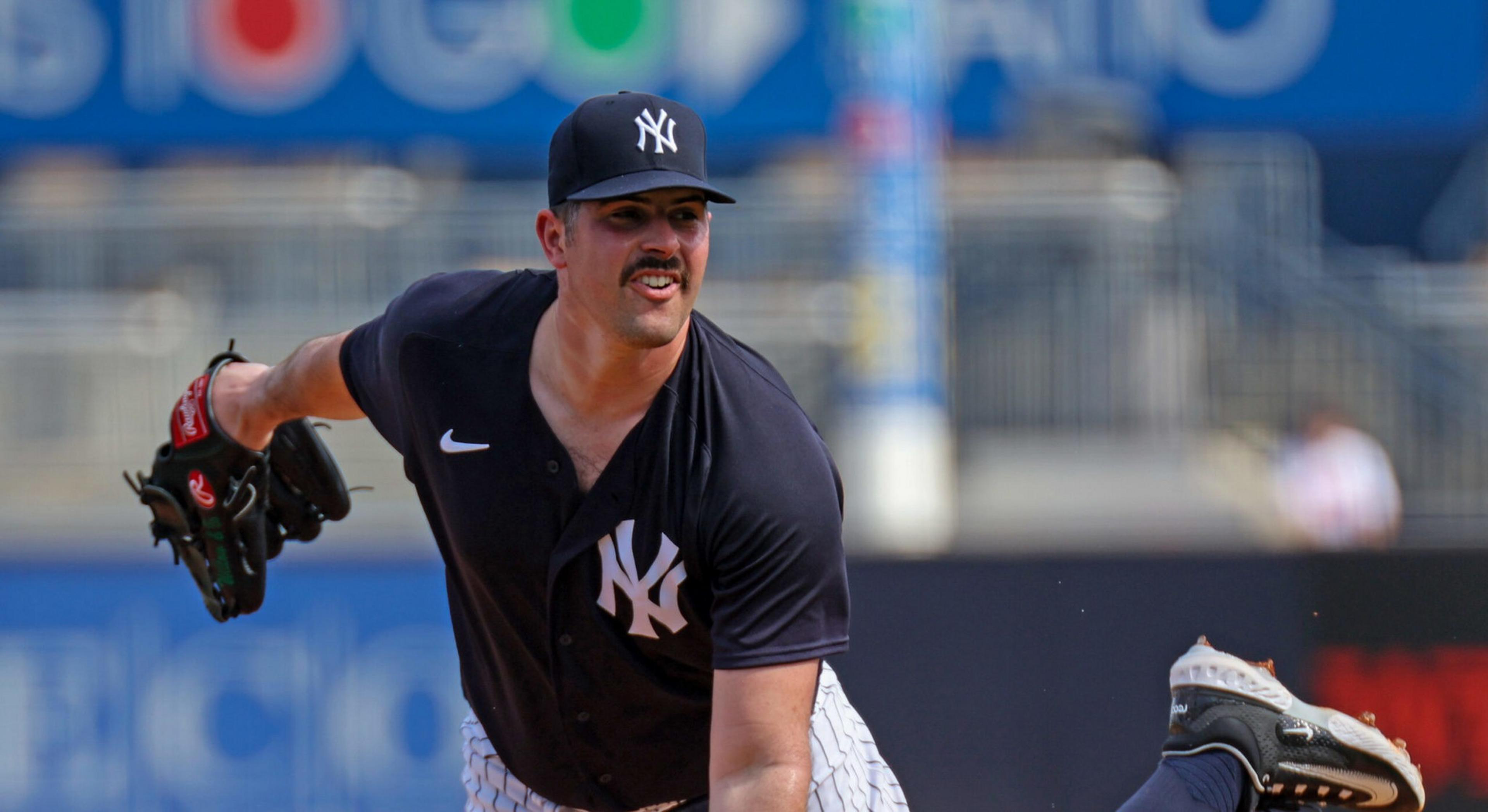 A baseball player in a New York Yankees cap and jersey is pitching the ball during a game, with one foot raised behind him.