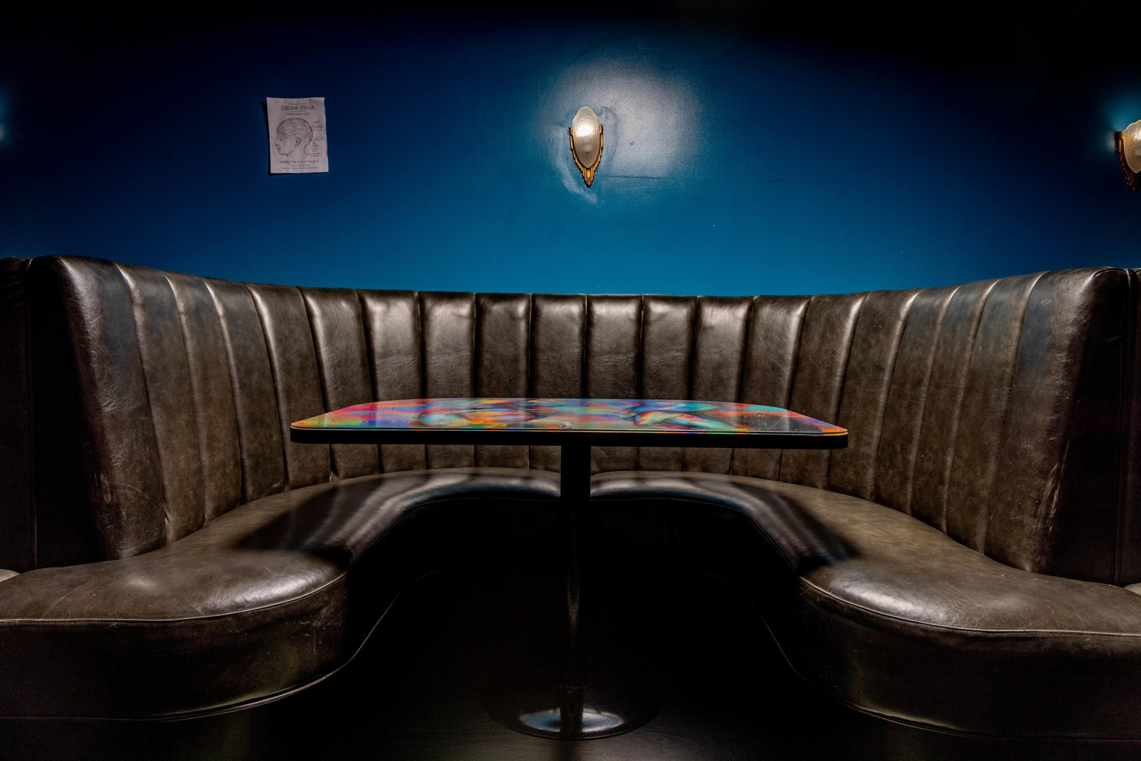 A warm brown booth with a colorful tabletop sits under a blue wall with a centered lighting fixture.