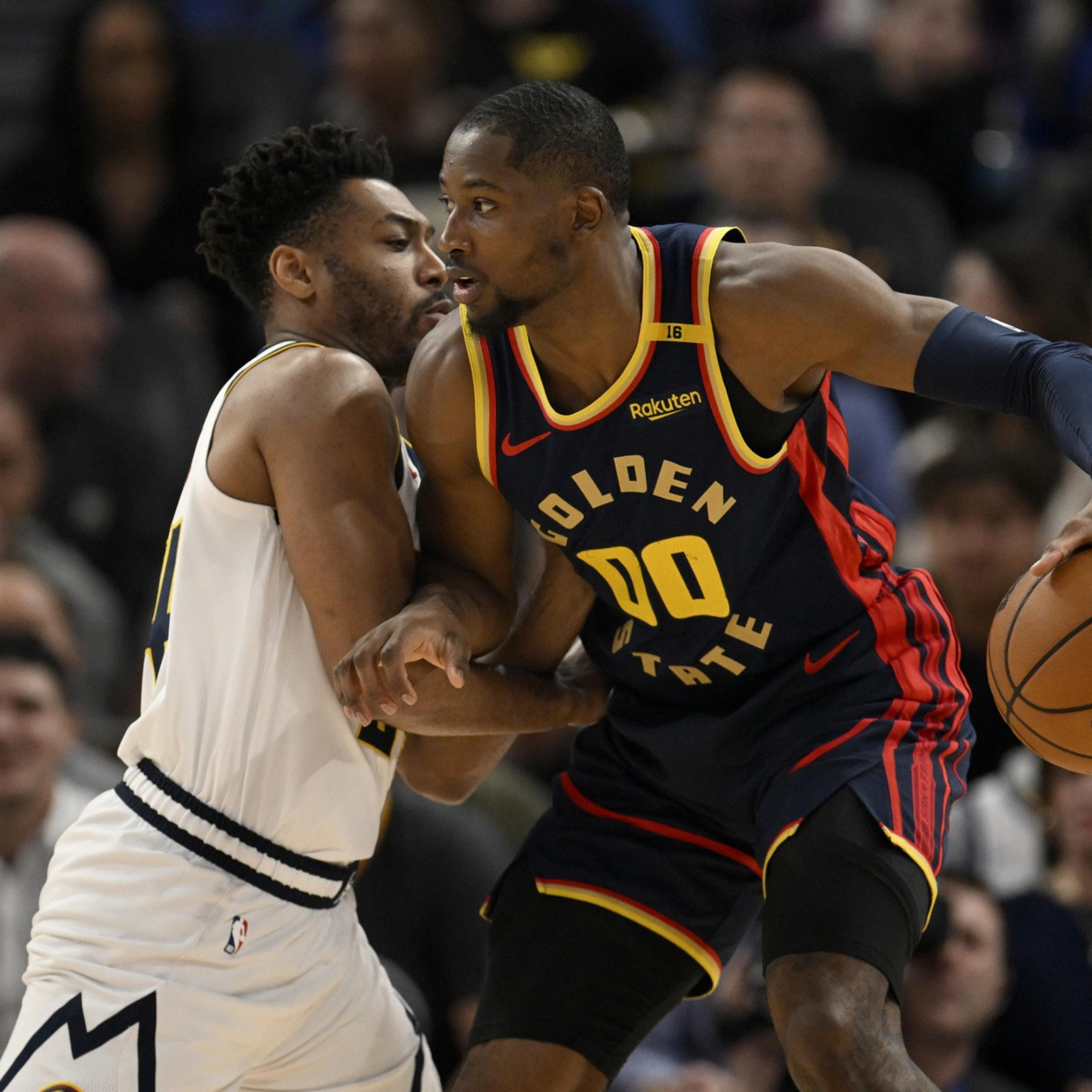 A Golden State Warriors player in navy and yellow holds a basketball while closely guarded by a defender in white during a game.
