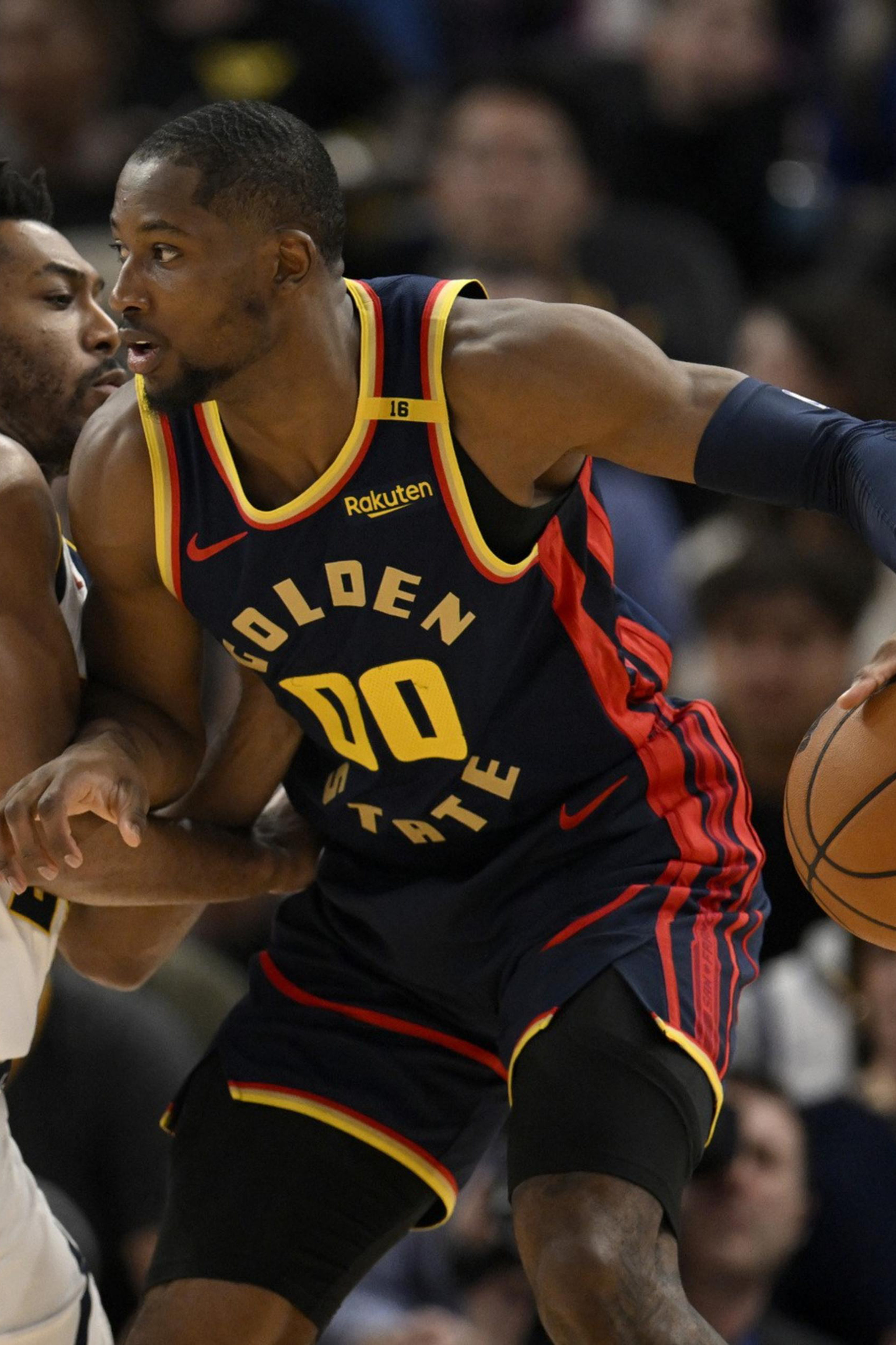 A Golden State Warriors player in navy and yellow holds a basketball while closely guarded by a defender in white during a game.