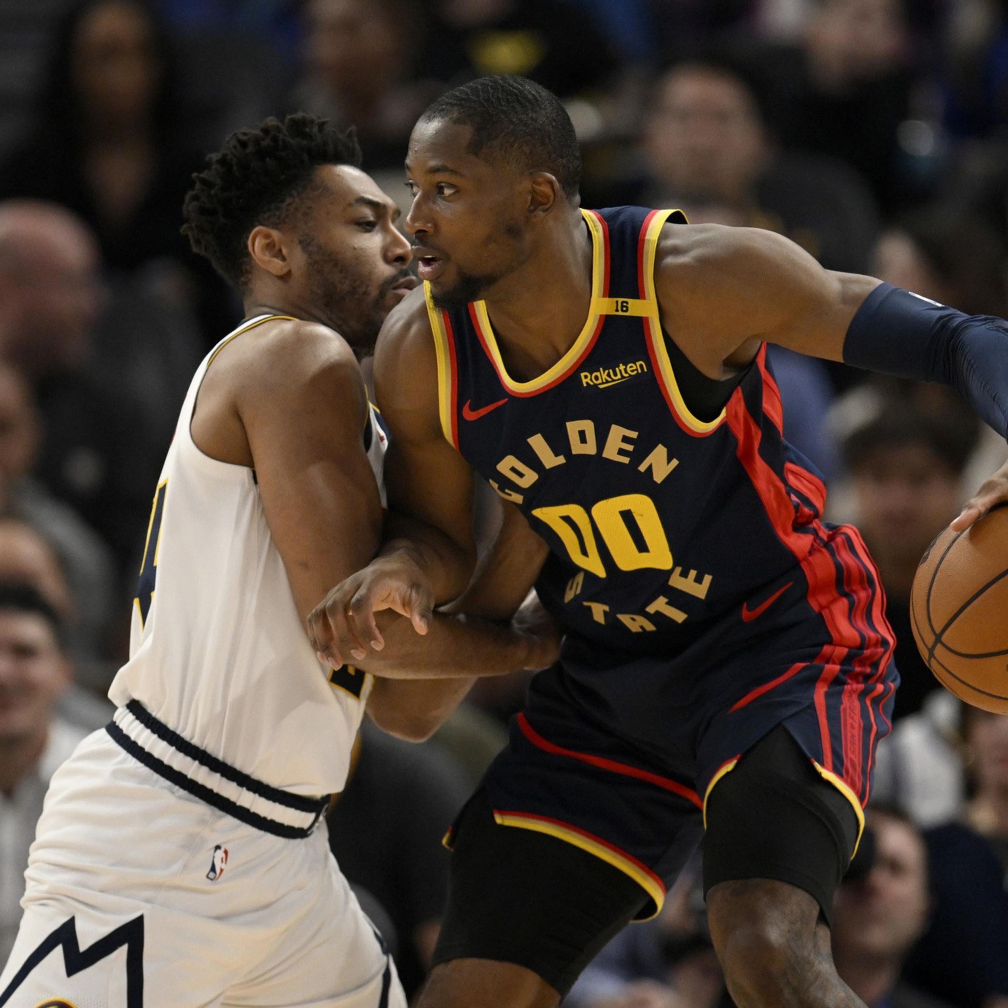 A Golden State Warriors player in navy and yellow holds a basketball while closely guarded by a defender in white during a game.