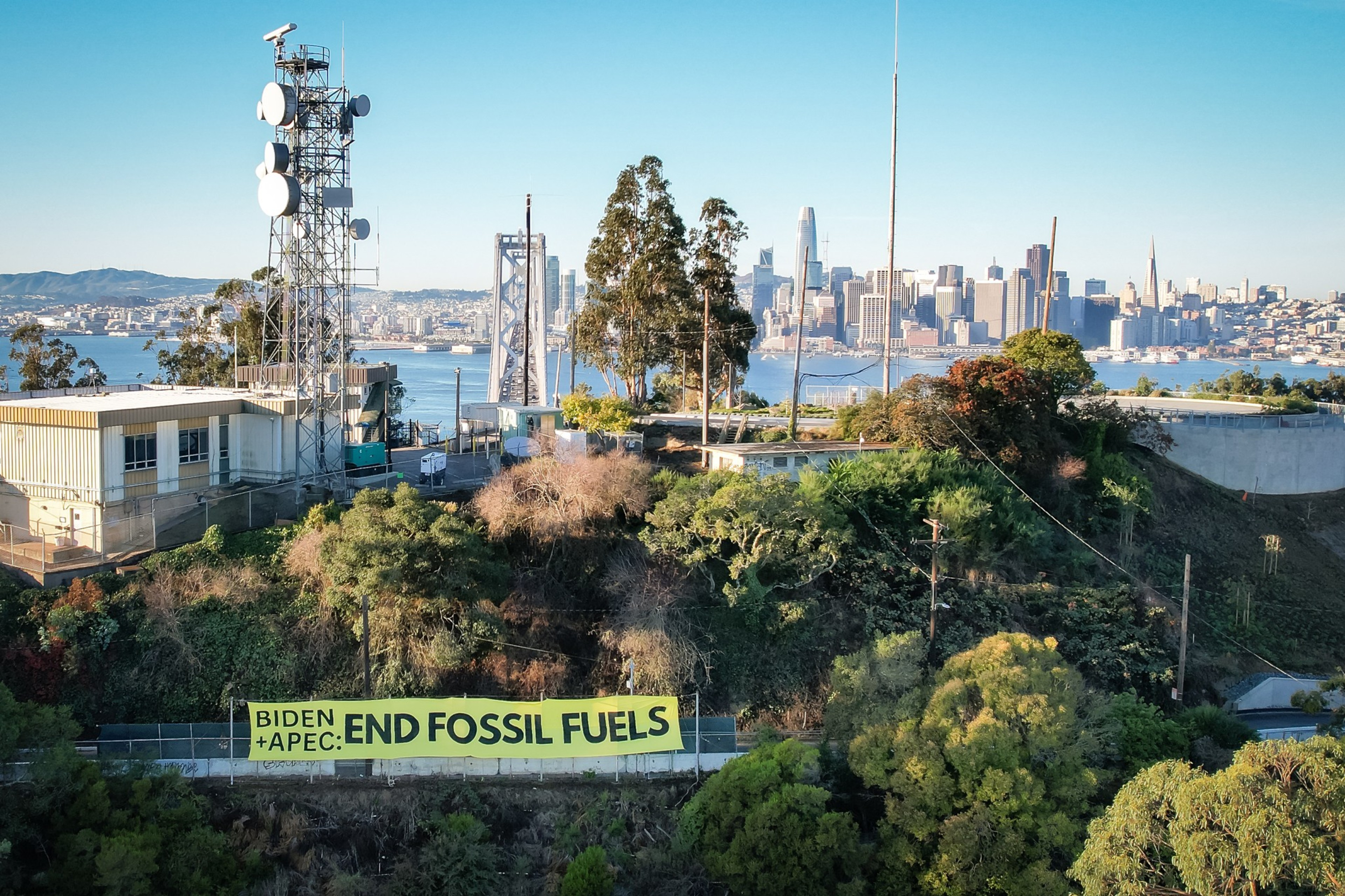 An aerial photo shows a large yellow banner reading &quot;Biden and APEC: End Fossil Fuels&quot; posted in front of buildings on San Francisco's Yerba Buena Island and a view of the city's skyline.