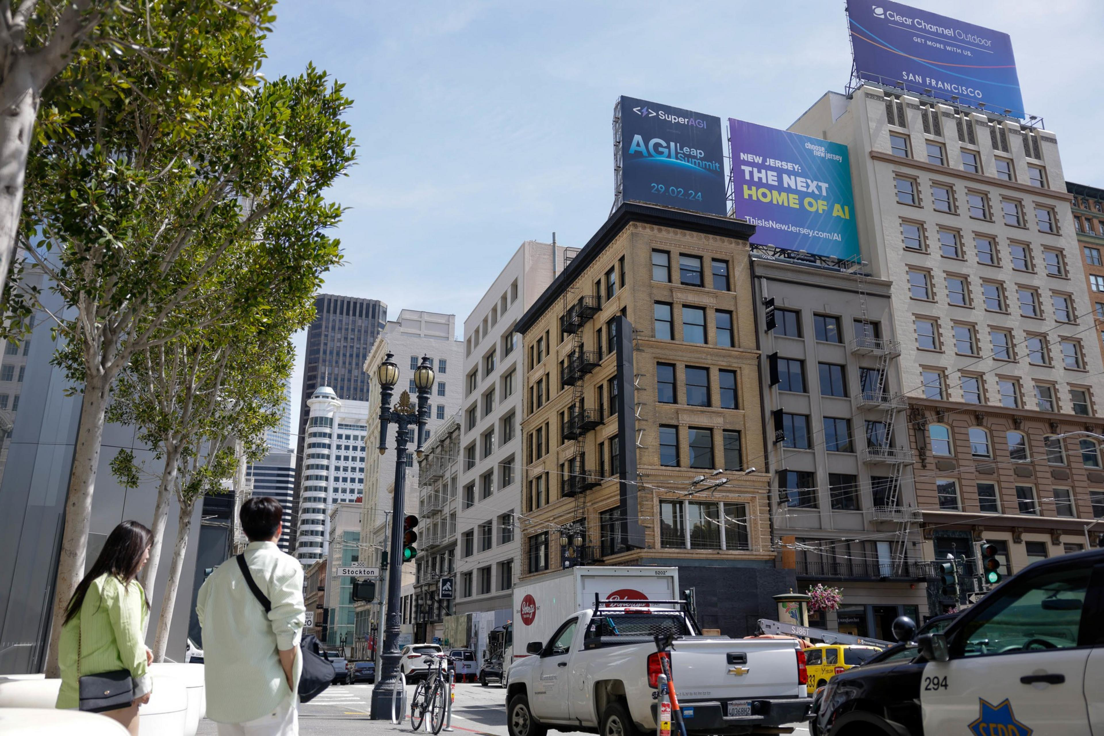 City street with buildings, vehicles, pedestrians, and billboards under a blue sky.