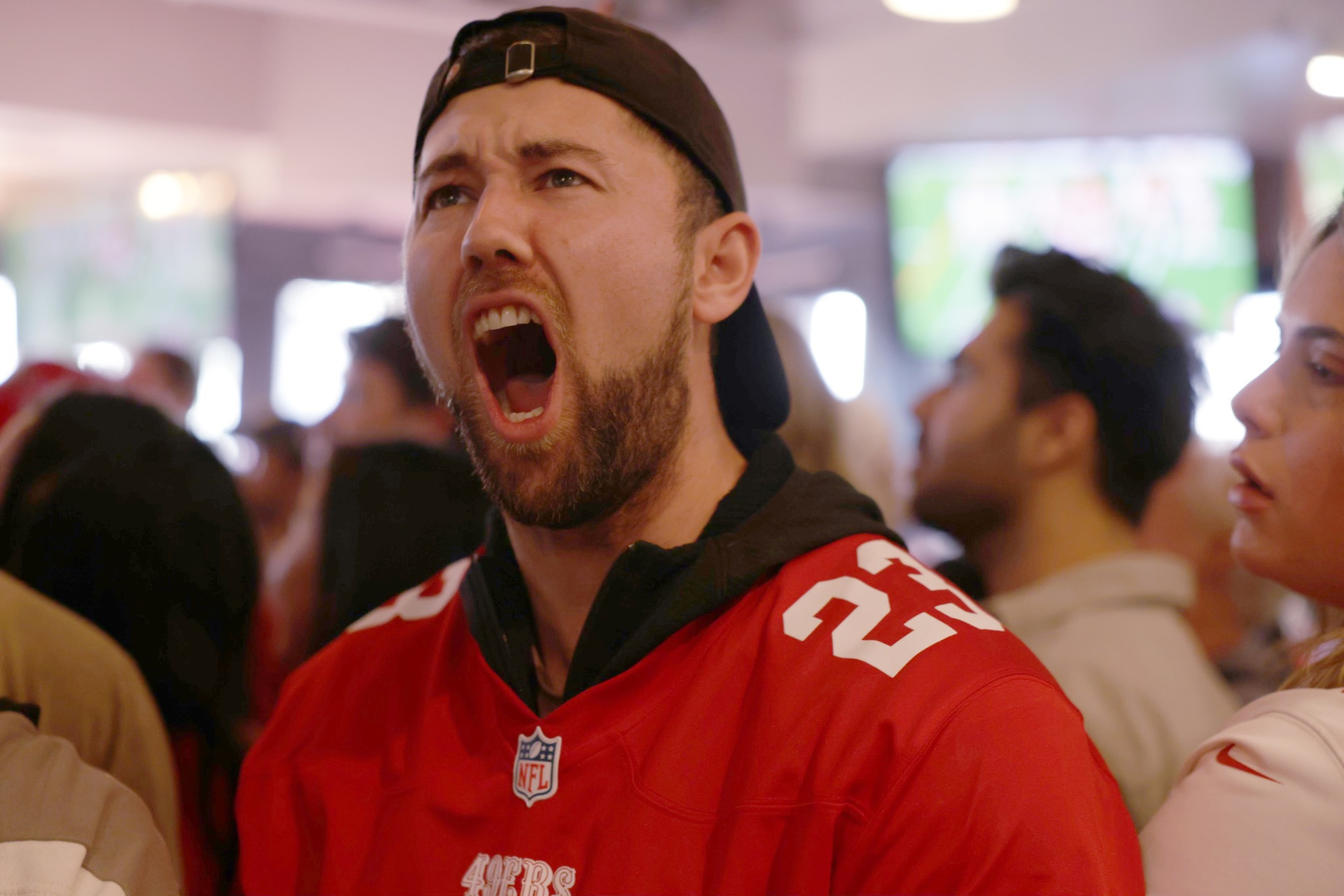 Man wearing backwards cap screams inside bar