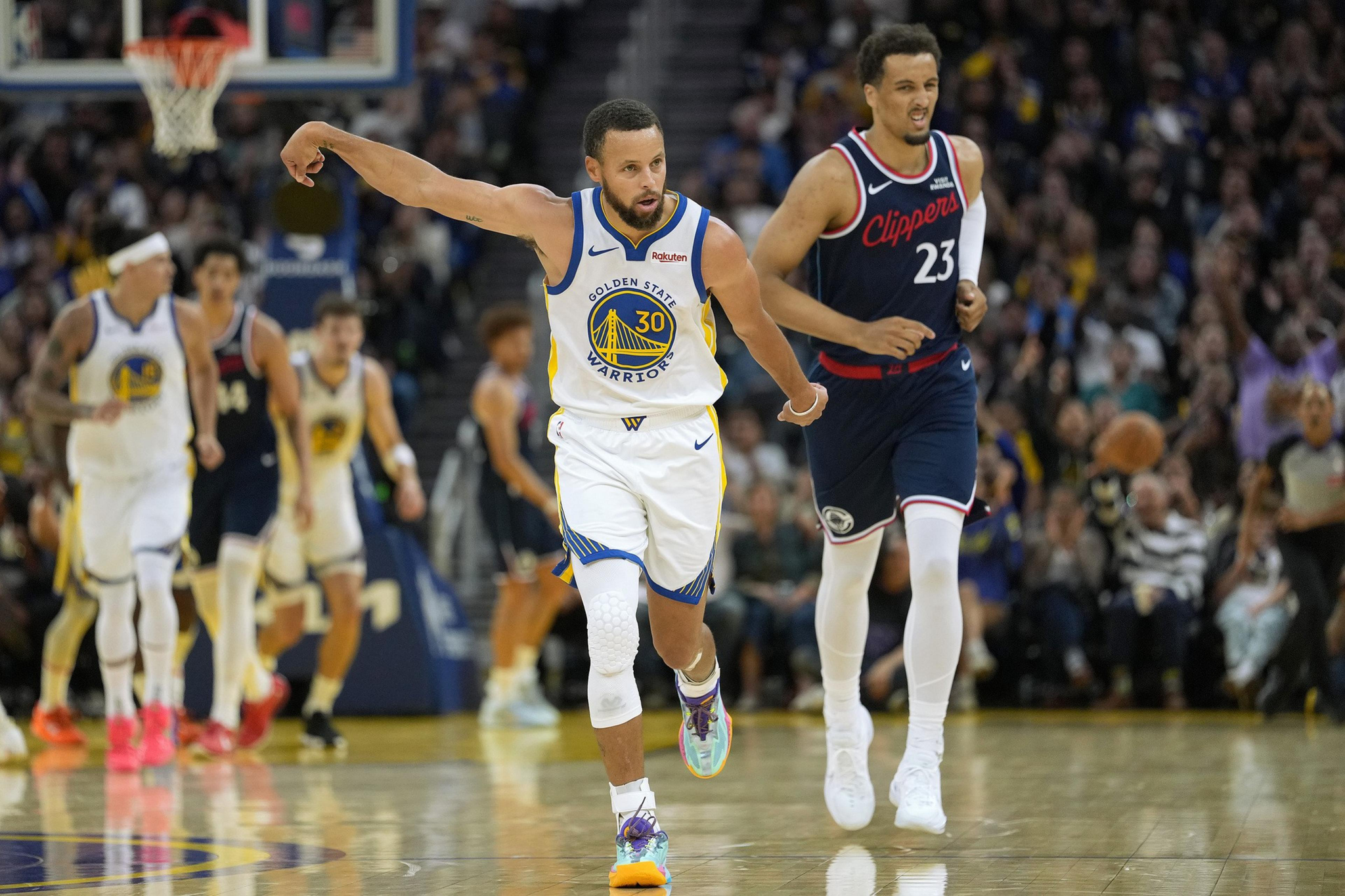 A Golden State Warriors player celebrates with an arm raised while a Clippers player runs behind him during a basketball game.