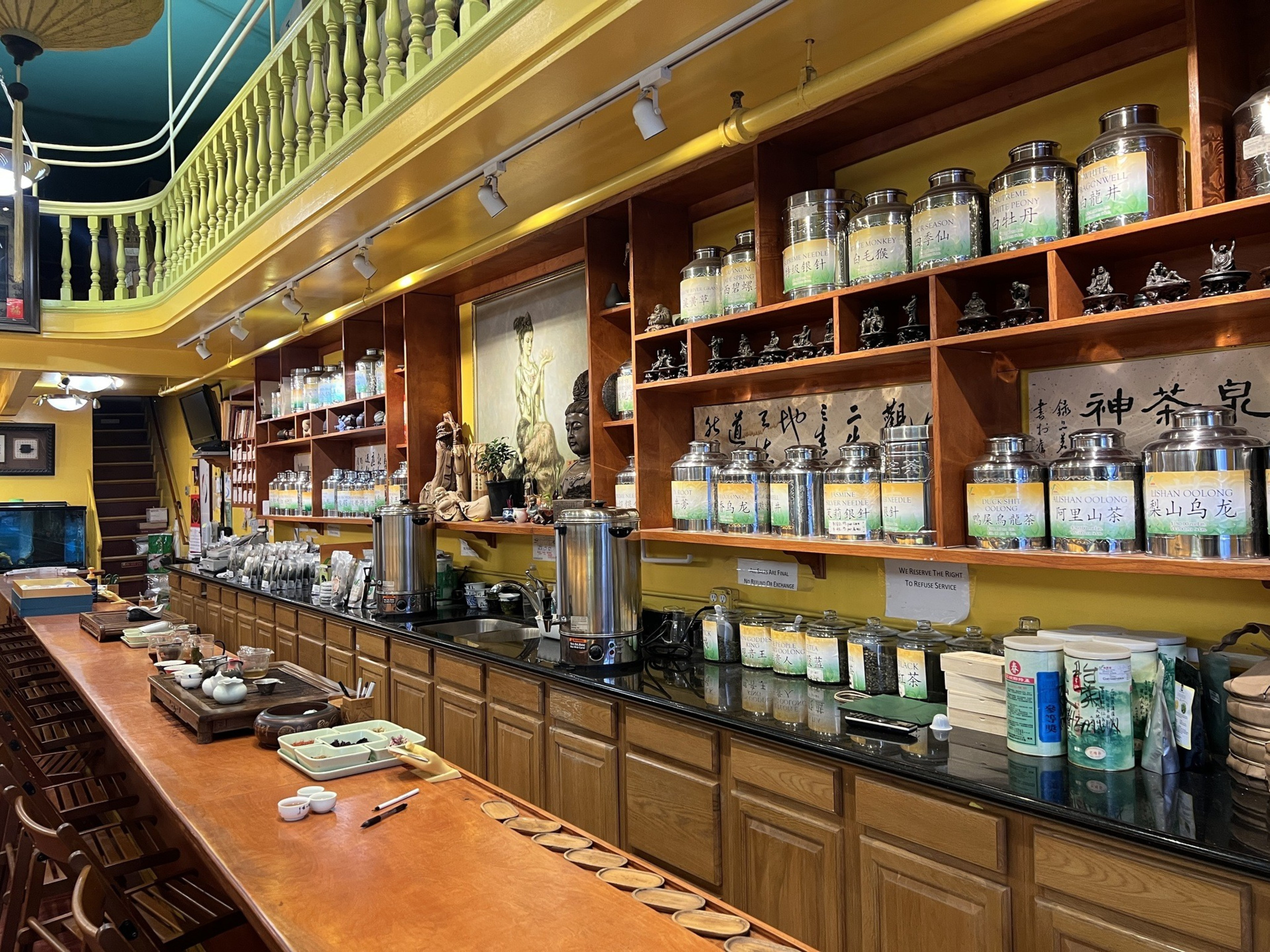 A long shelf with a counter in front of it holds metal canisters of tea.
