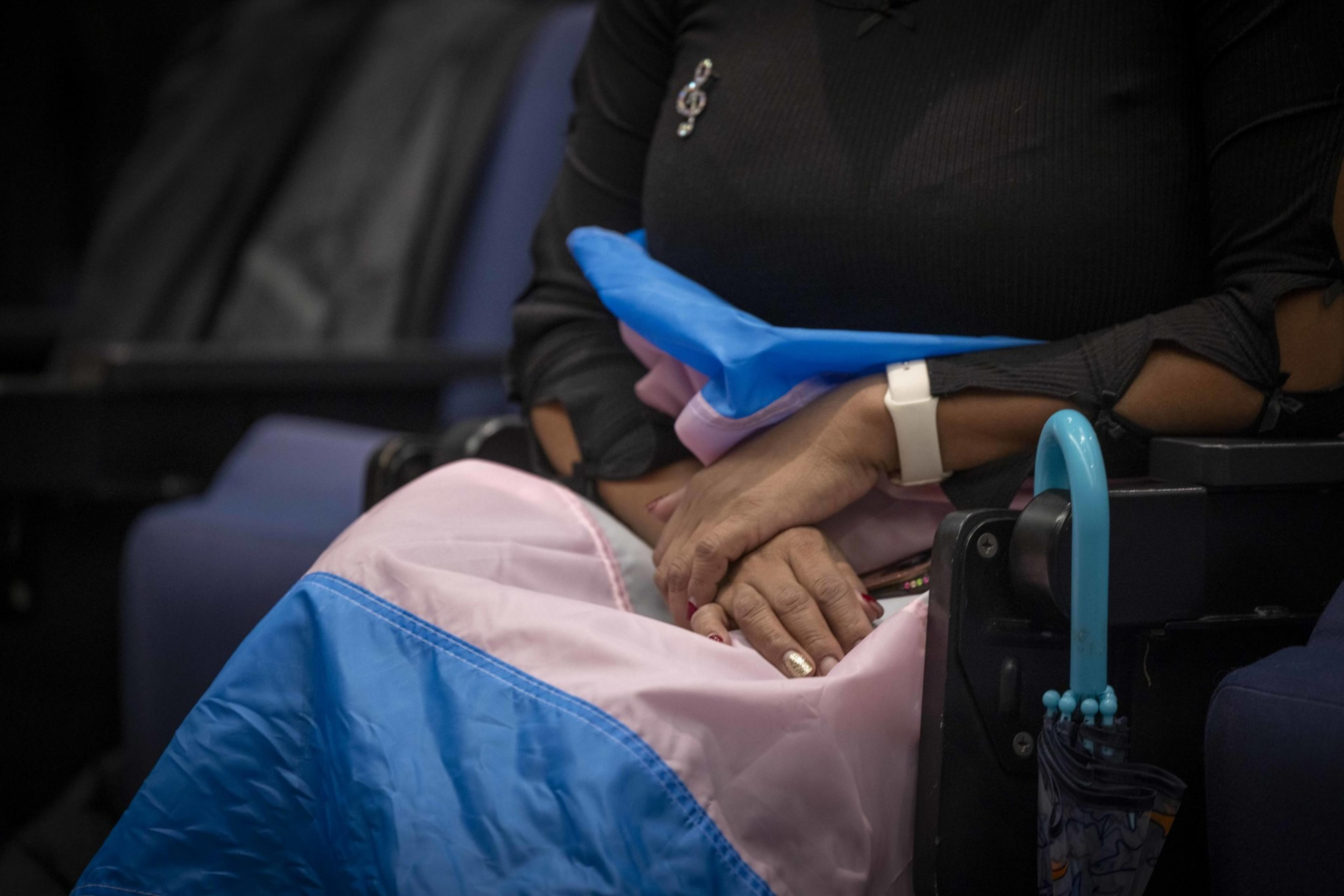 A closeup of hands draped over a transgender community flag on someone's lap.