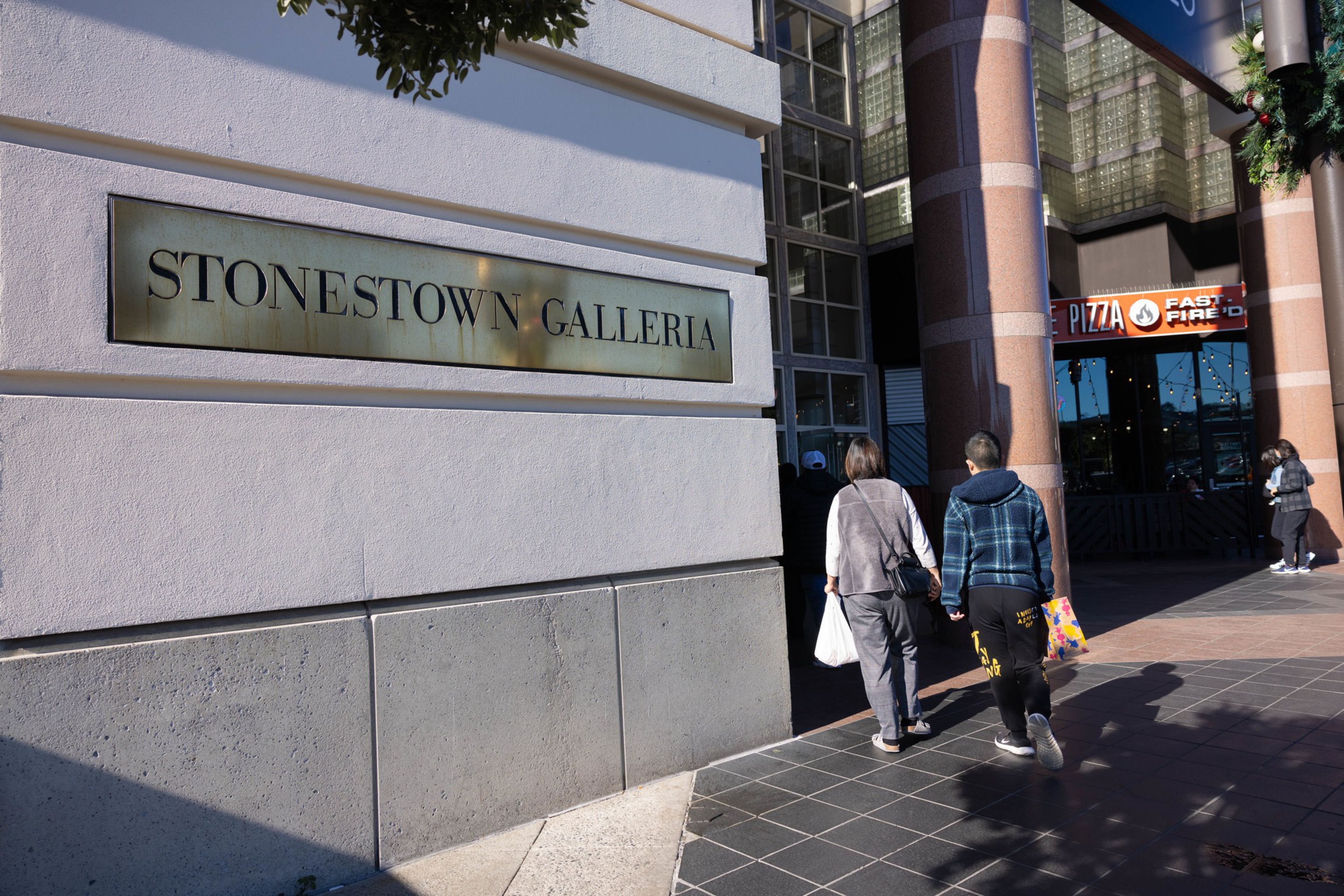The exterior or Stonestown Galleria with two people walking toward the entrance.