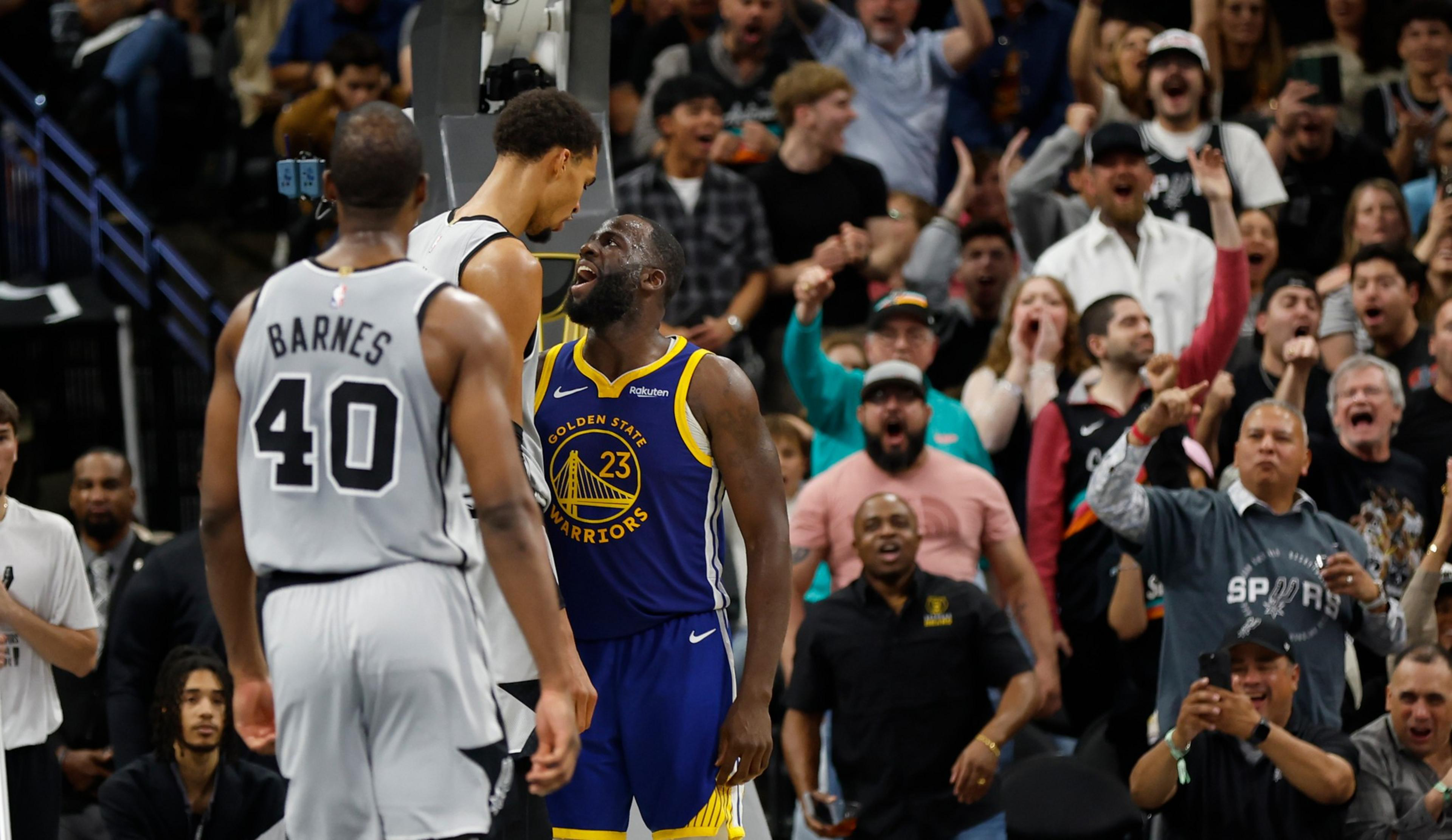 A Golden State Warriors player passionately confronts a San Antonio Spurs player, as an excited crowd cheers loudly behind them.